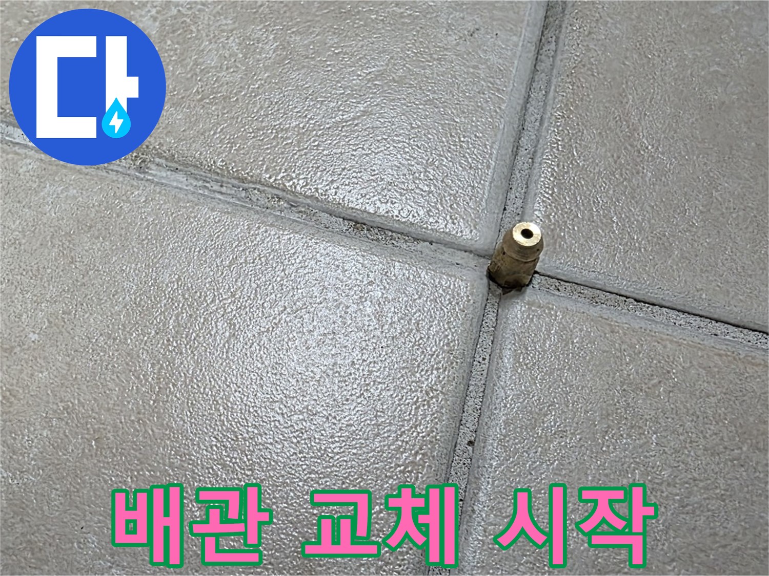 회색 타일 사이의 금속 배관 연결 부품 모습입니다.