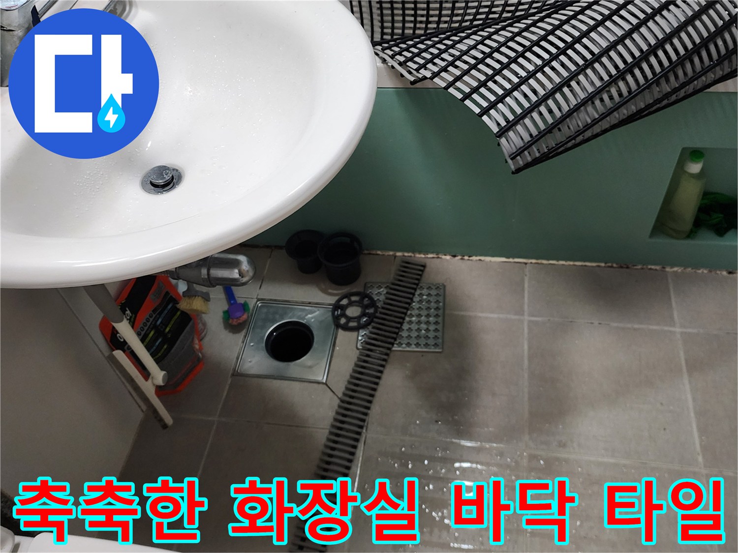 세면대 밑 공간의 젖은 바닥 타일과 배수구 모습