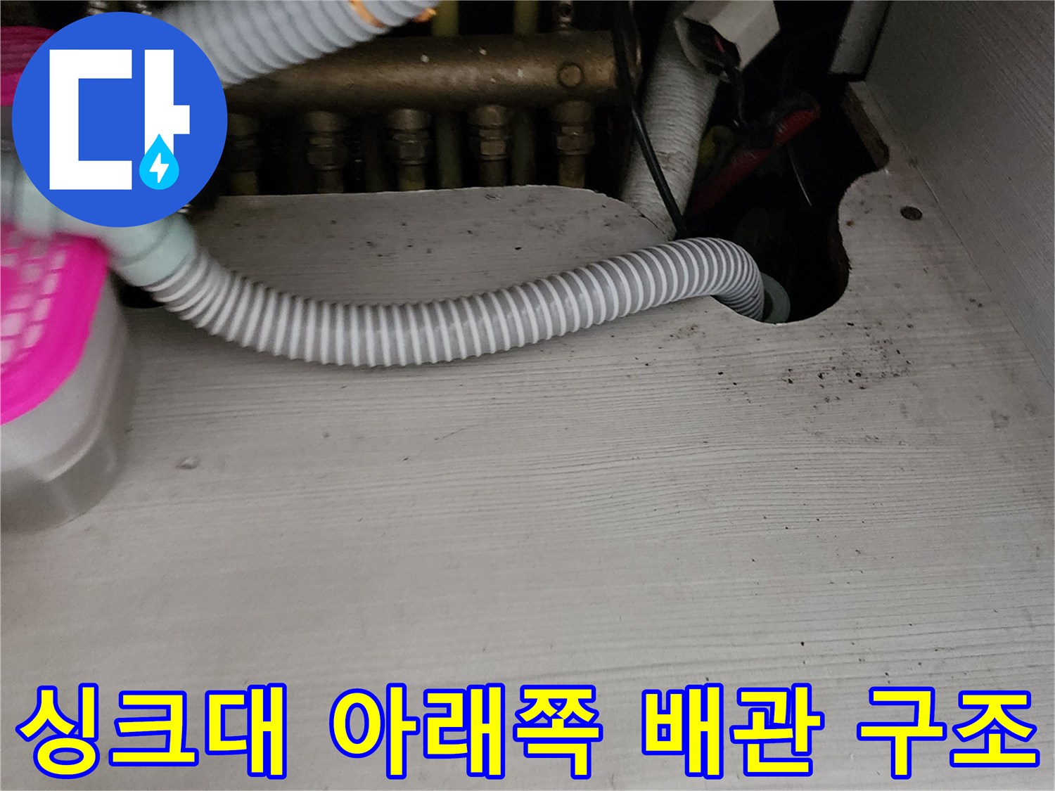 싱크대 하부장 내부의 배수 호스와 금속 관로 모습