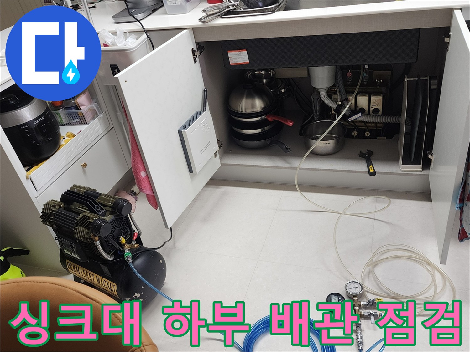 주방 싱크대 하부장 내부의 배관 연결 상태와 압력 테스트 장비 모습