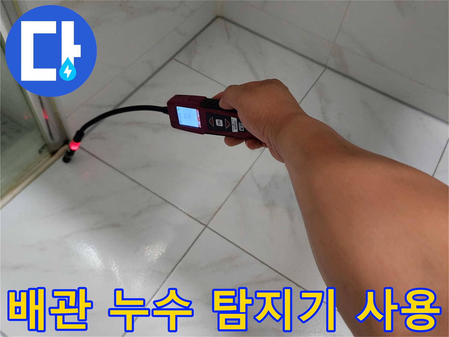 밝은 톤의 타일 벽면에 가스 탐지기를 대고 검사하는 손과 장비