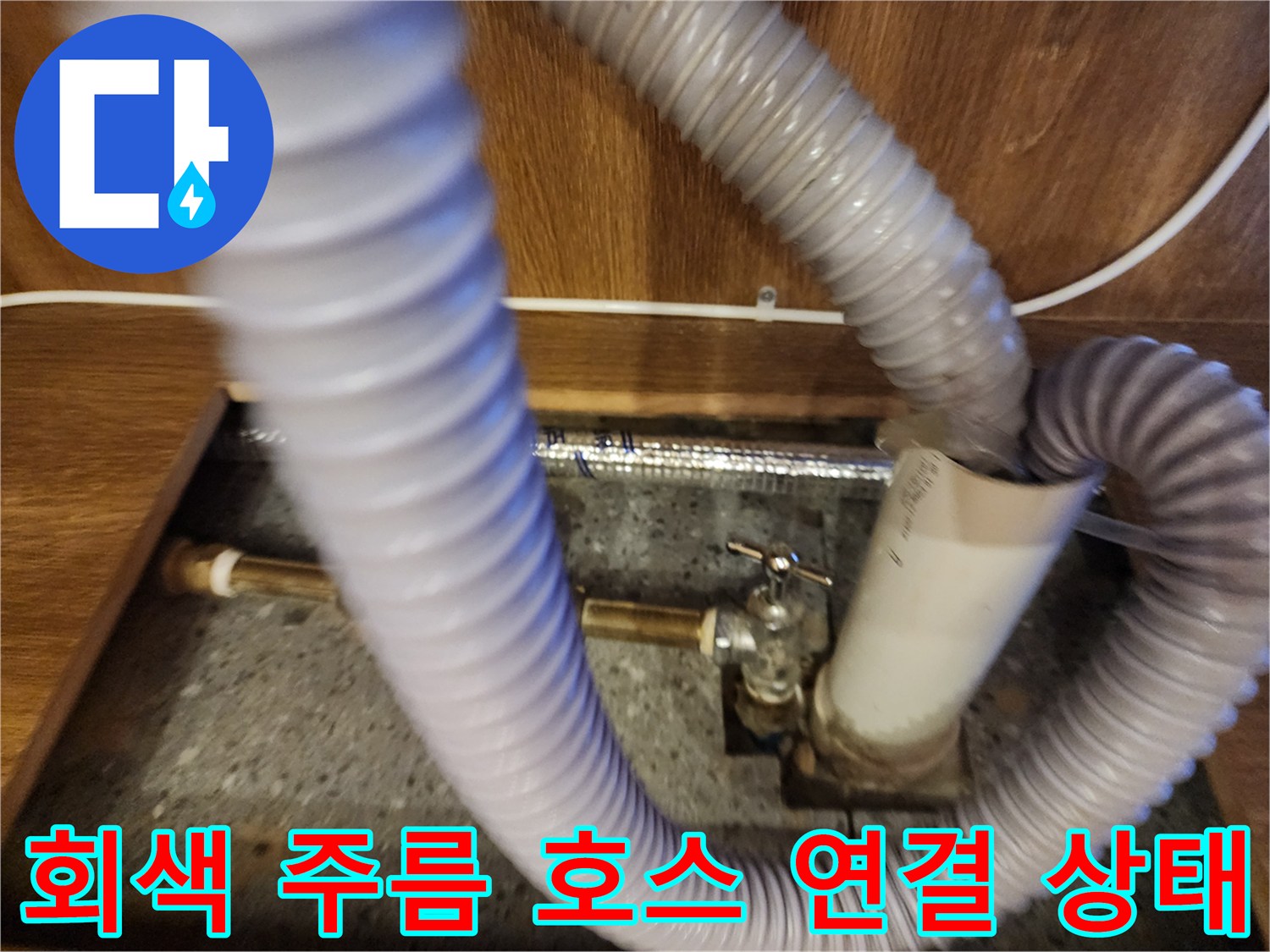 주방 싱크대 밑에 설치된 유연한 회색 호스와 수직 배관