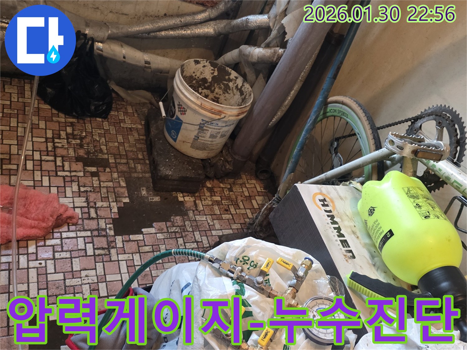 배관 누수 지점을 찾기 위해-압력 게이지와 호스가 연결된-전문 탐지 장비가 사용되는 장면입니다.