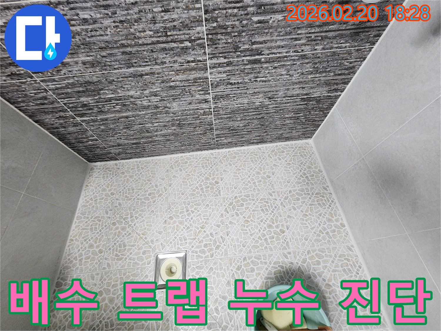 장안동 욕실의 배수 트랩 주변 바닥 타일을 촬영한 이미지입니다-트랩 연결부의 누수 가능성을 염두에 두고-표면 상태를 면밀히 관찰하고 있습니다.