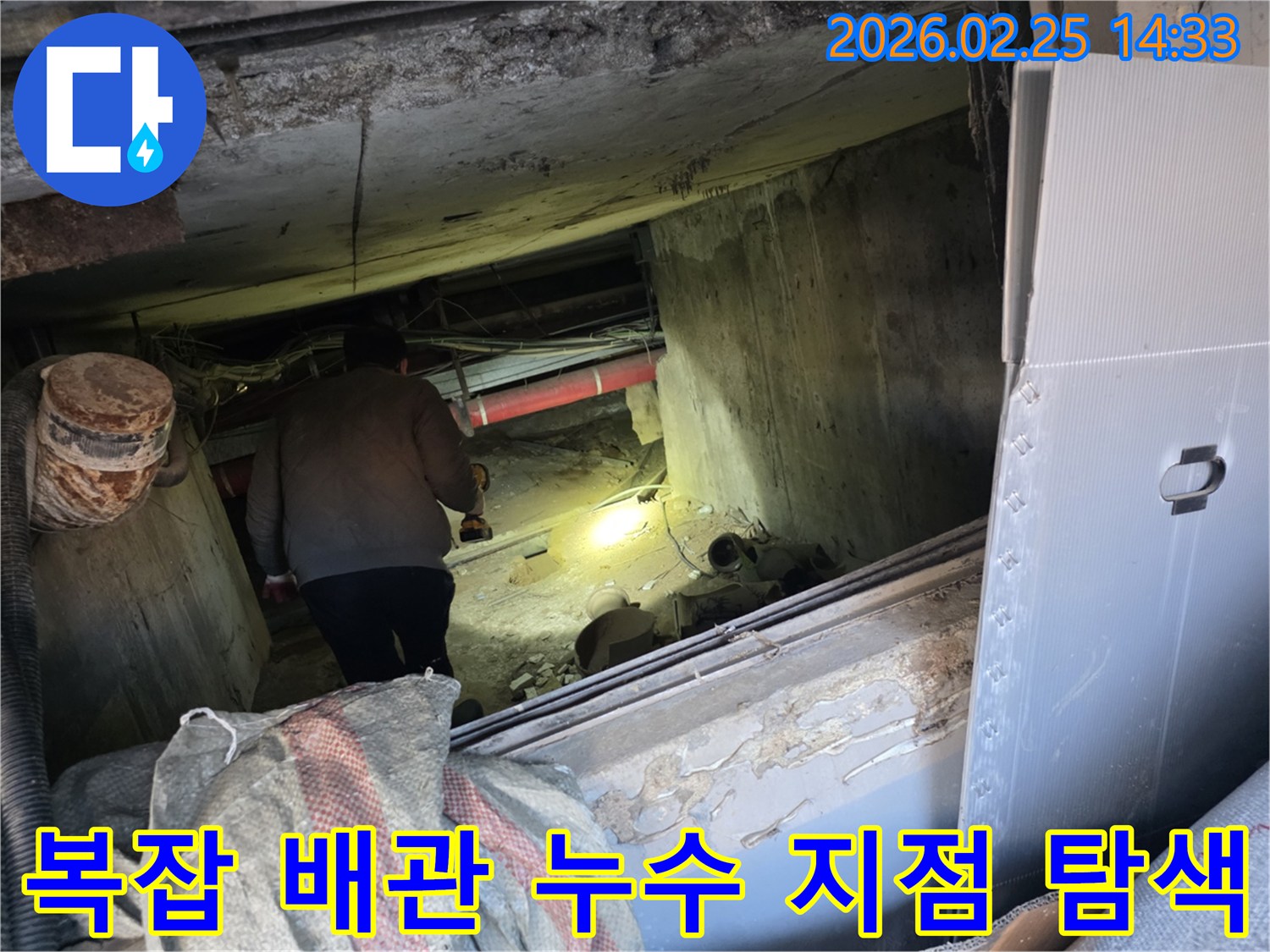 누수 전문 엔지니어가-어둡고 복잡한 배관이 얽힌 공간에서-손전등으로 구석구석을 비추며-누수 지점을 정밀하게-탐색하는 전문적인 모습입니다.