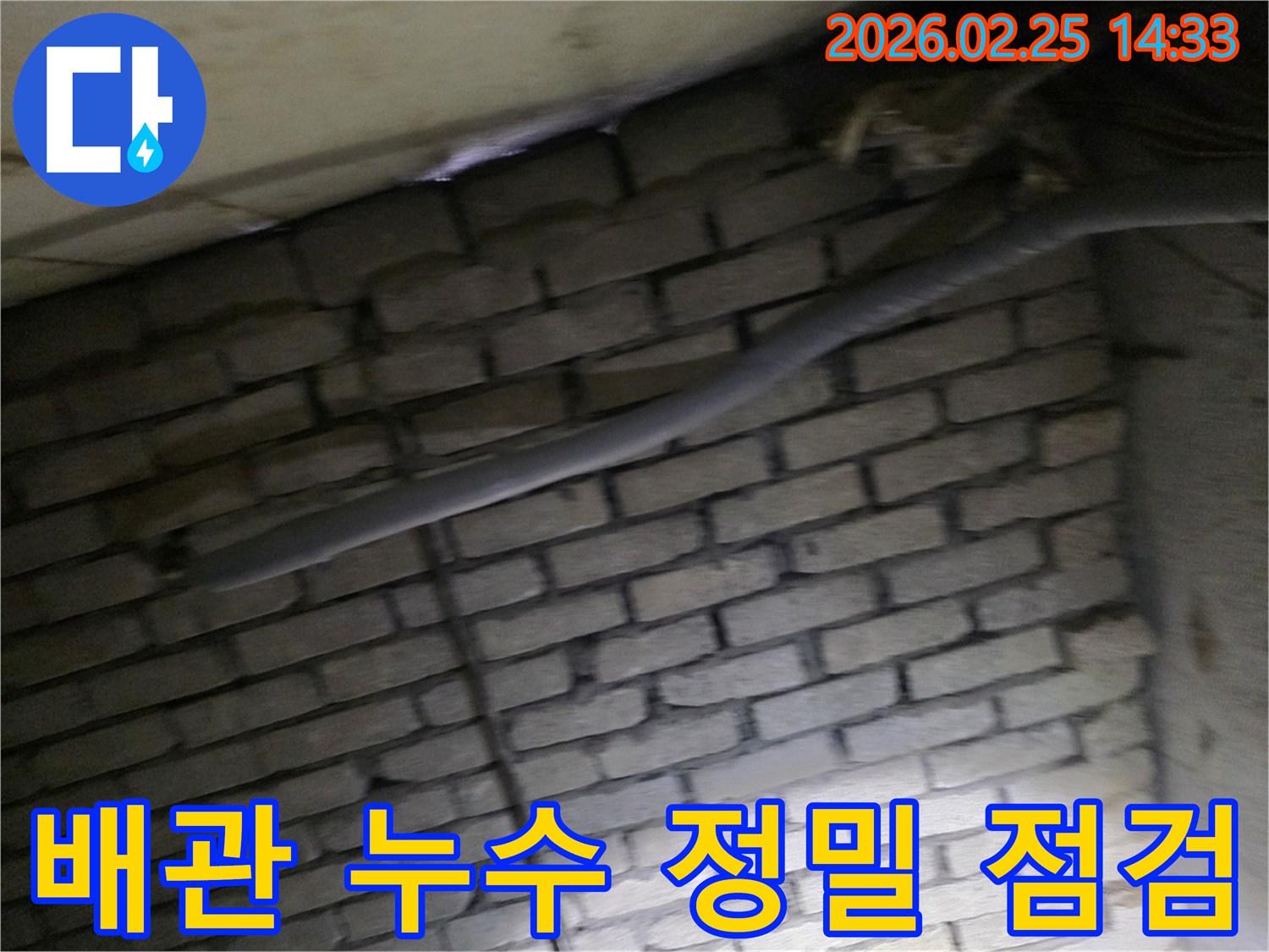 어두운 벽돌 벽면을 배경으로-단열된 배관과 함께-누수 여부를 정밀하게-점검하는 현장 모습입니다.