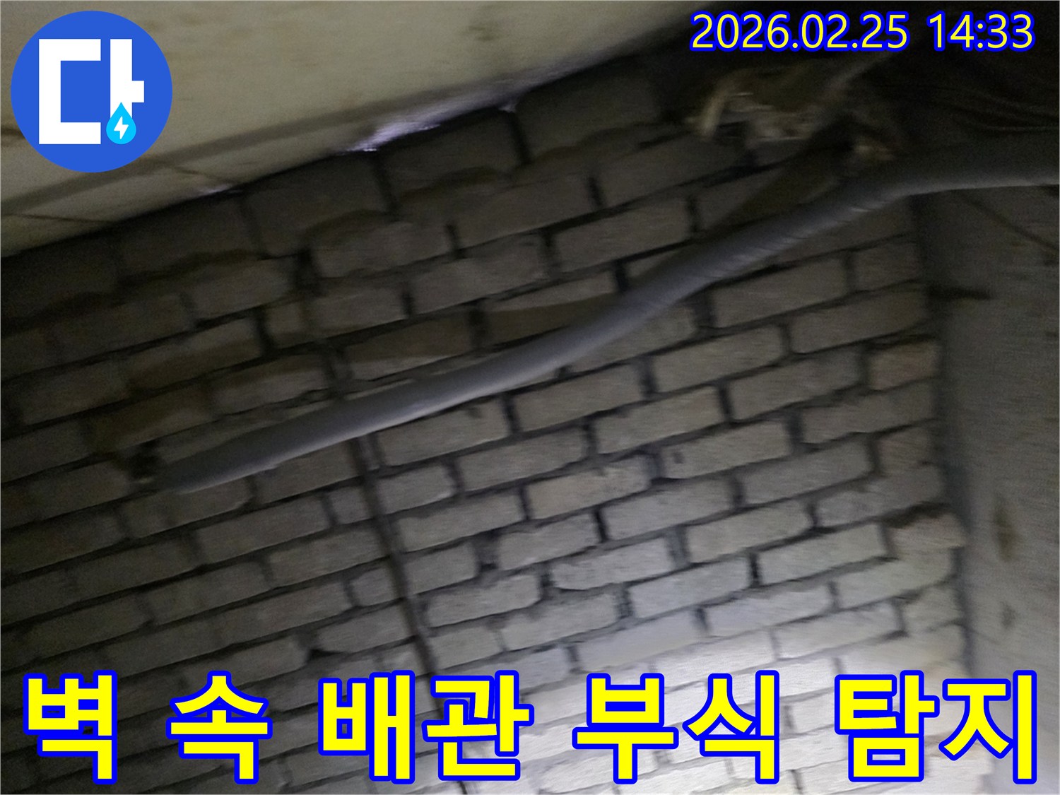 어두운 벽돌 벽면을 배경으로-오래된 배관의 부식 여부를-확인하기 위해 촬영된 현장 사진입니다.