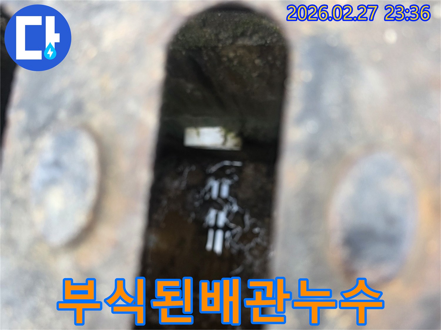녹슨-철제-덮개-아래-고인-물과-물속에-잠긴-부식된-배관의-일부가-선명하게-보이는-누수-현장