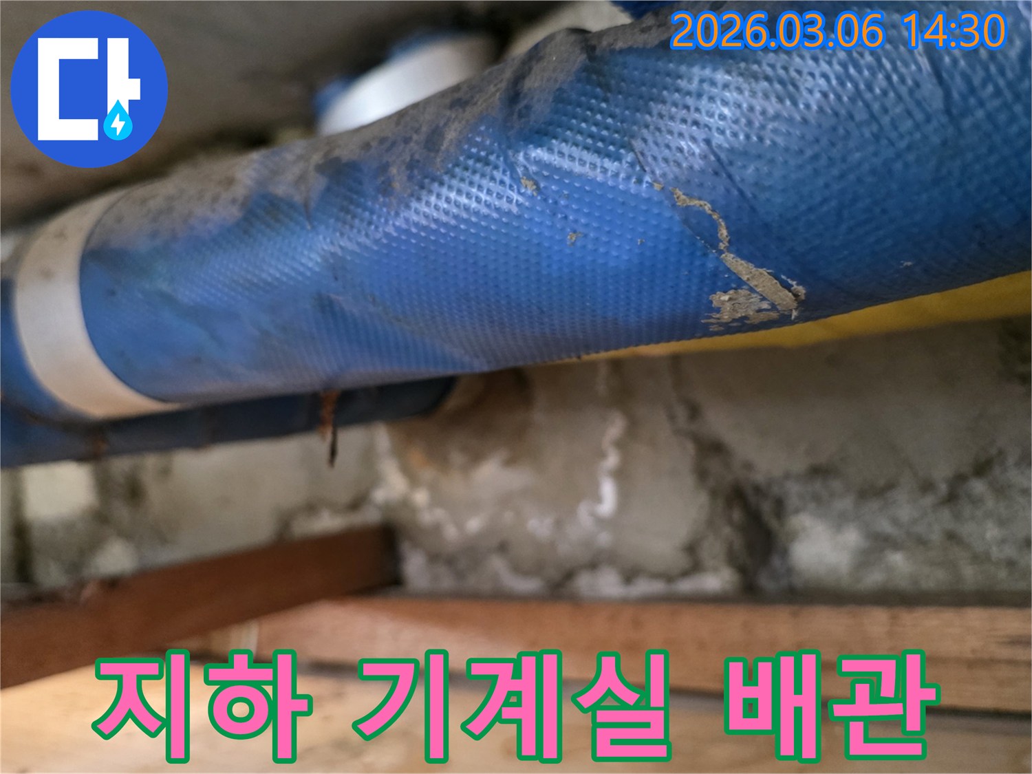 아파트 지하 기계실의-파란색 배관과-젖은 콘크리트 벽면-그리고 나무 지지대를-꼼꼼히 점검하는 모습