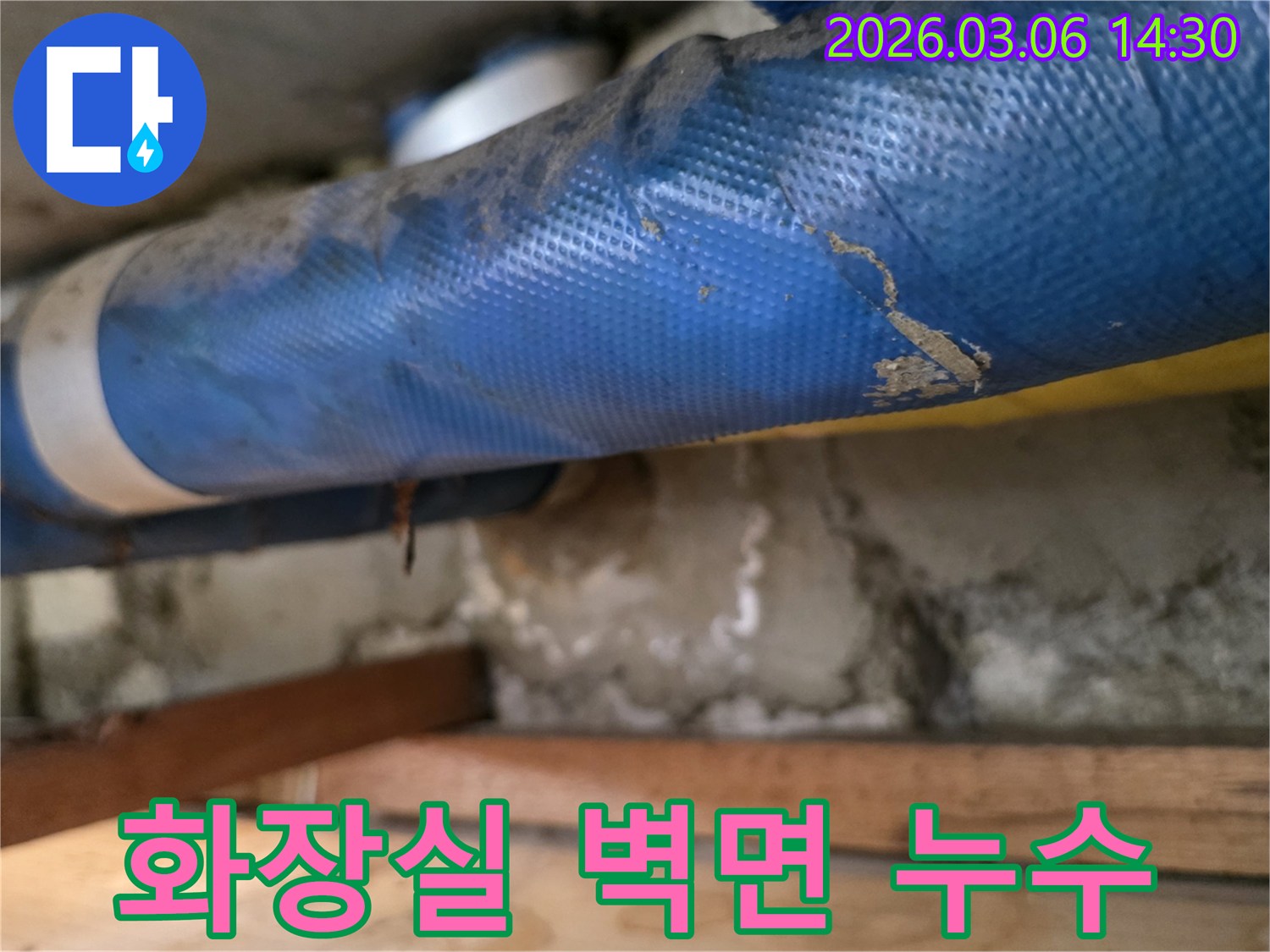 아파트 화장실 벽면-파란색 배관과-젖은 콘크리트 벽면-그리고 나무 지지대를-꼼꼼히 점검하는 모습