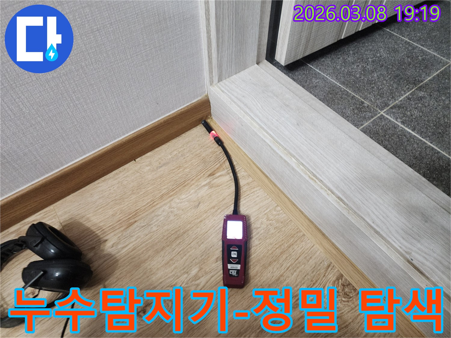 나무-바닥과-벽면-경계에서-누수탐지기가-붉은색-불빛으로-누수-위치를-지목하는-사진
