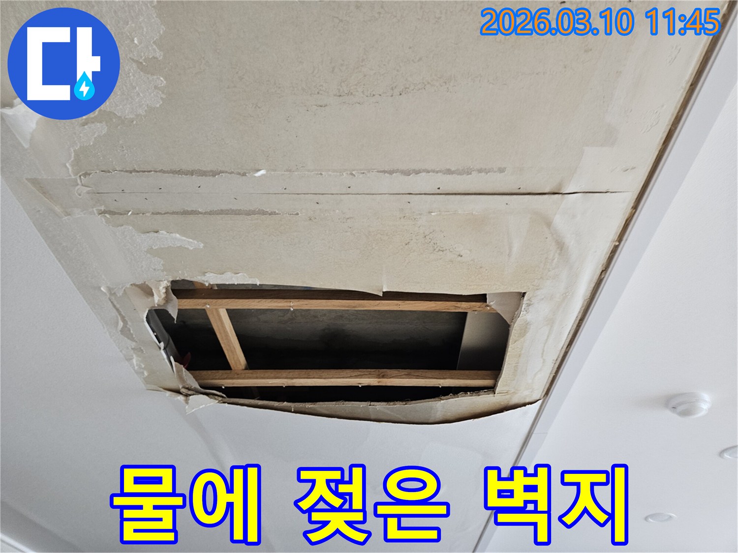 오래된 누수로 인해-벽지가 젖고 훼손되어-천장 내부의-목재 구조물이-드러난 현장 사진입니다.
