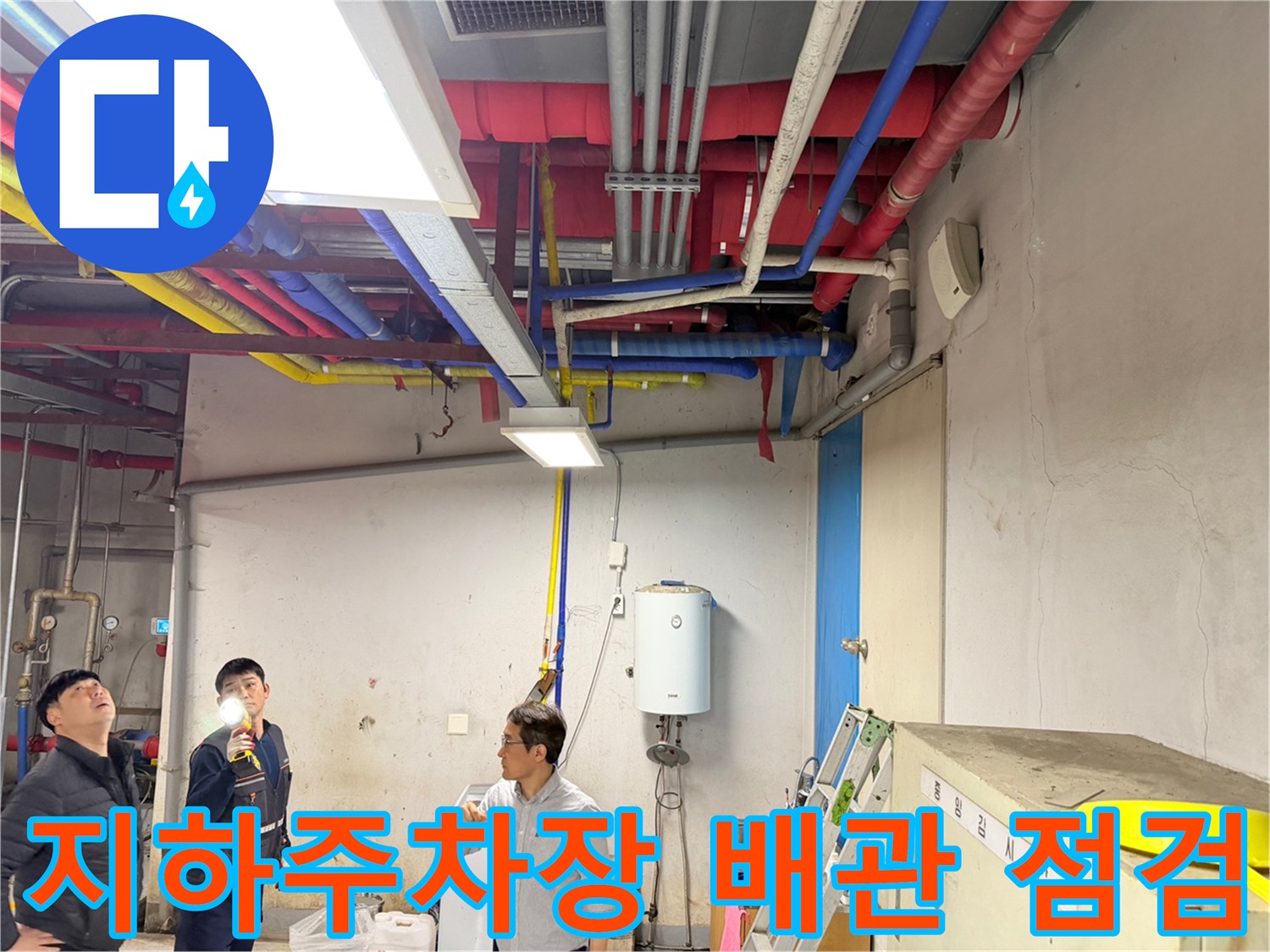 지하 주차장 천장의 복잡한 배관 라인을 엔지니어가 손전등으로 조사하고 있습니다.
