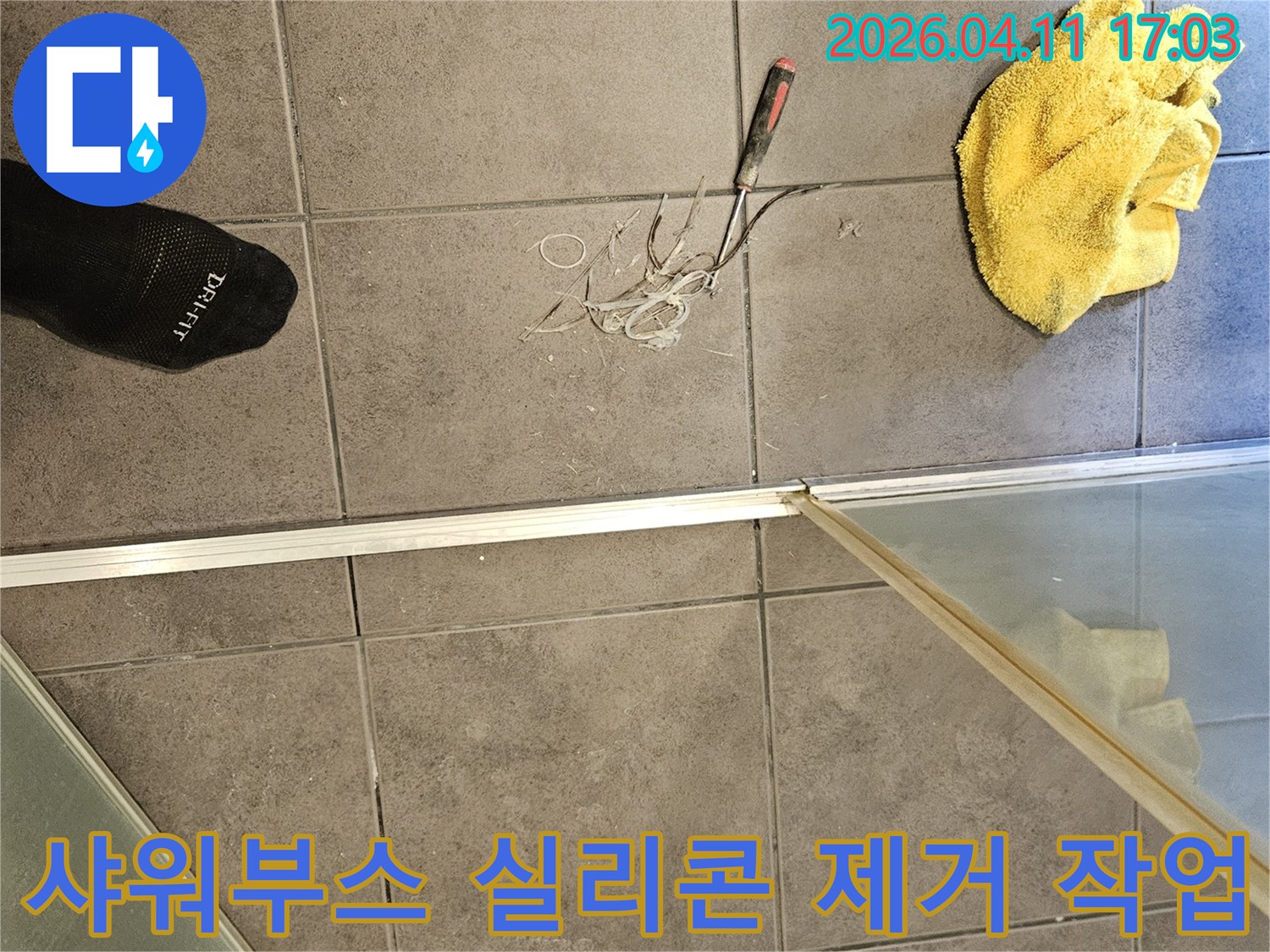 욕실 바닥에 놓인 노란 수건과-공구-그리고 샤워부스 경계면의 낡은 실리콘을 긁어내는 현장 사진