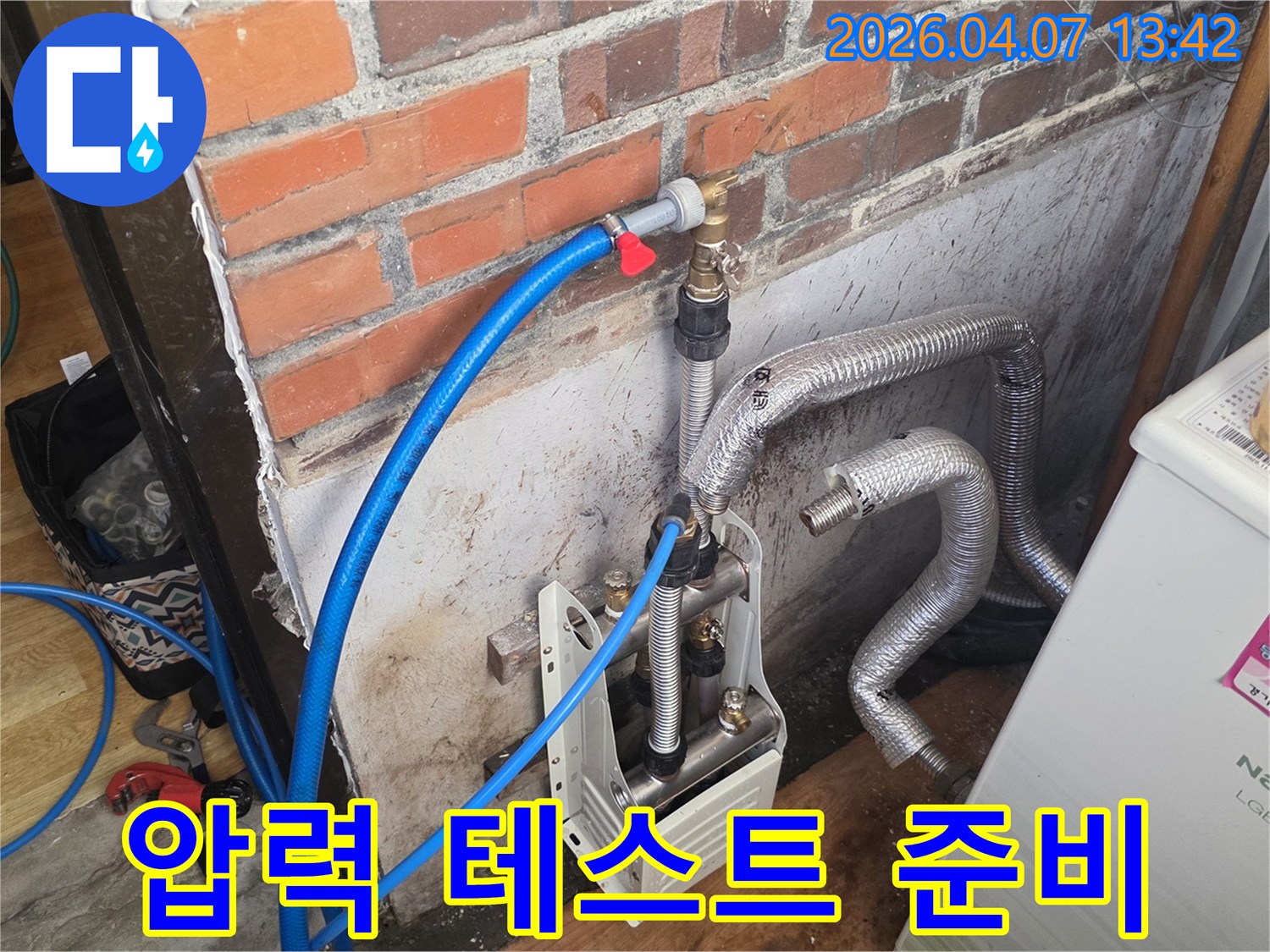 벽돌 벽 옆에-누수 탐지 장비가-설치되어 있으며-파란색 호스를 통해-배관에 압력을 가하기 위한-준비가 진행 중입니다.