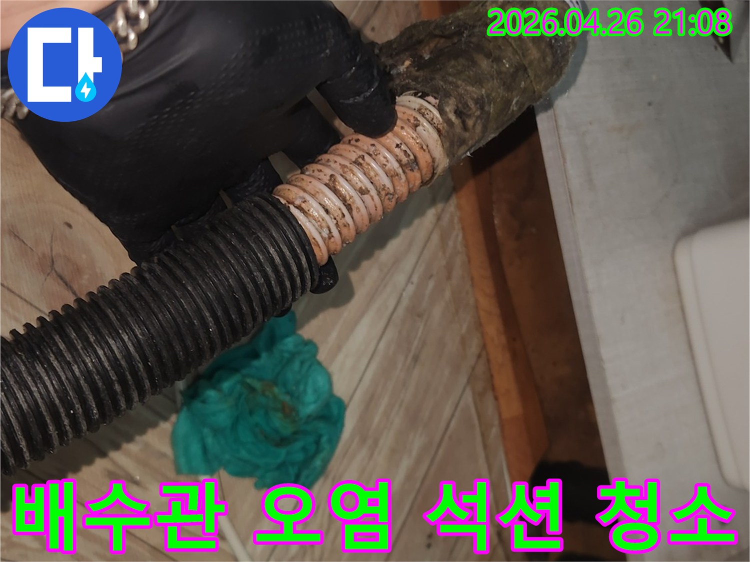 검은 장갑을 착용한 기술자가-오염된 싱크대 배수 호스를-석션 장비로 꼼꼼하게 청소하여-누수와 악취를 예방하는 모습