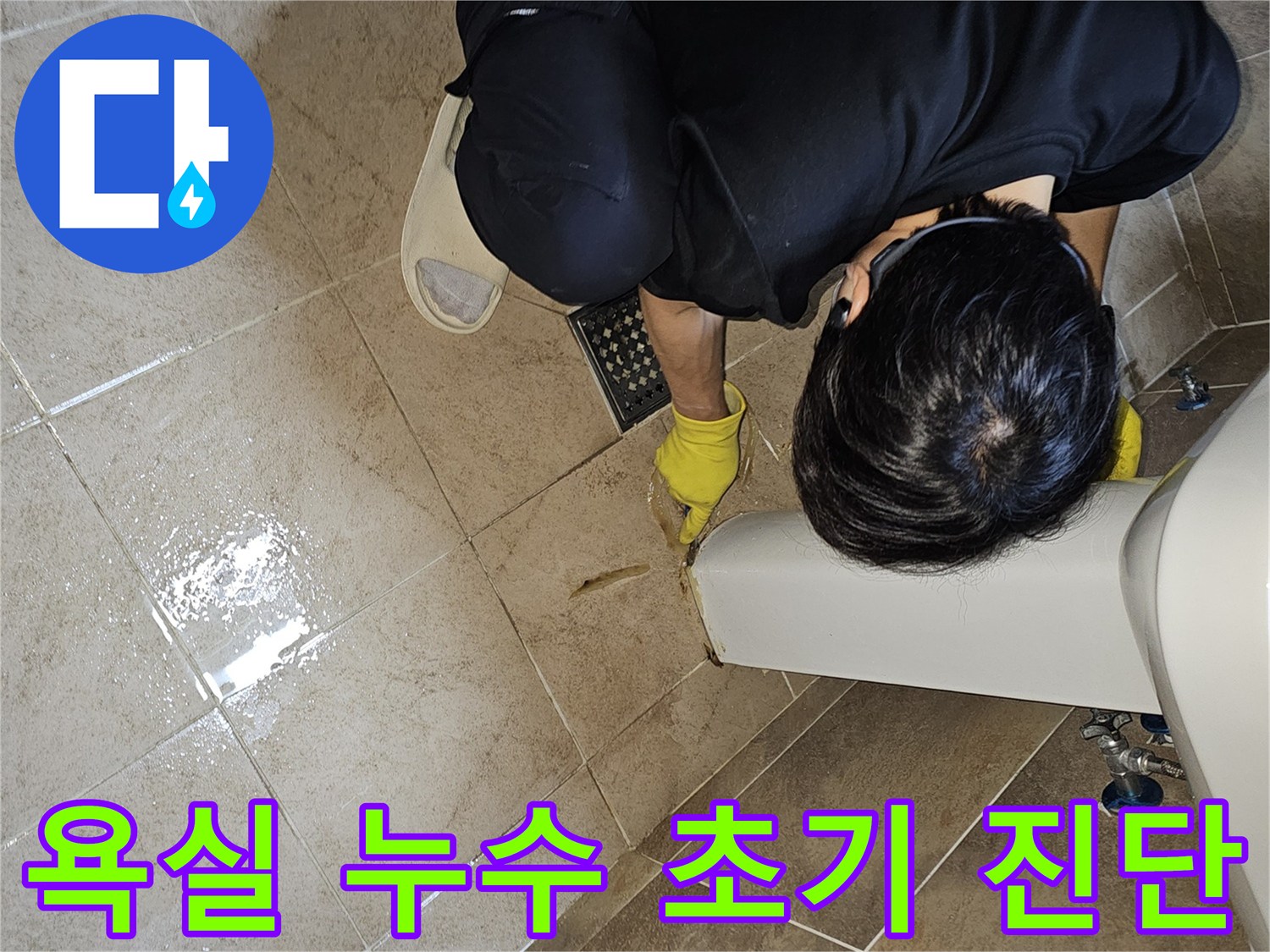 누수 전문가가-노란 장갑을 끼고-욕실 바닥의 젖은 타일과-세면대 하단부를-집중적으로 관찰하며-누수 지점을 파악하고 있습니다