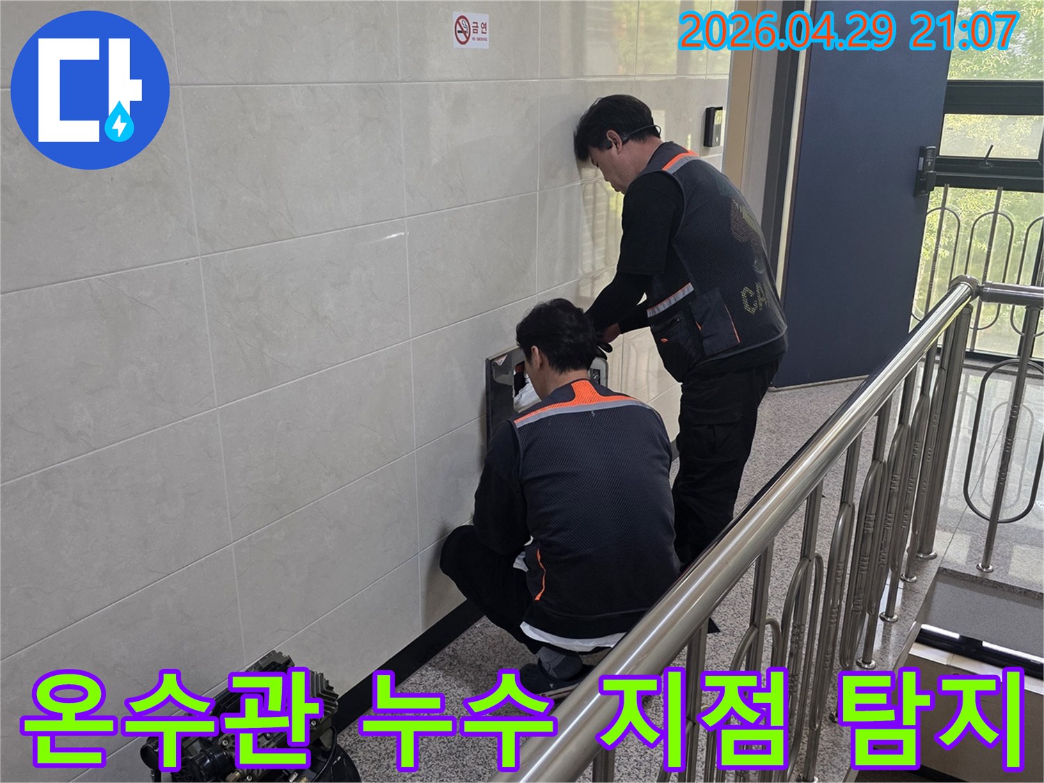 두 명의 전문 기술자가 건물 벽면 내부의 온수관 누수 의심 지점을 정밀하게 탐지하고 있습니다-난방비 절감과 쾌적한 환경 조성을 위한 필수 작업입니다.