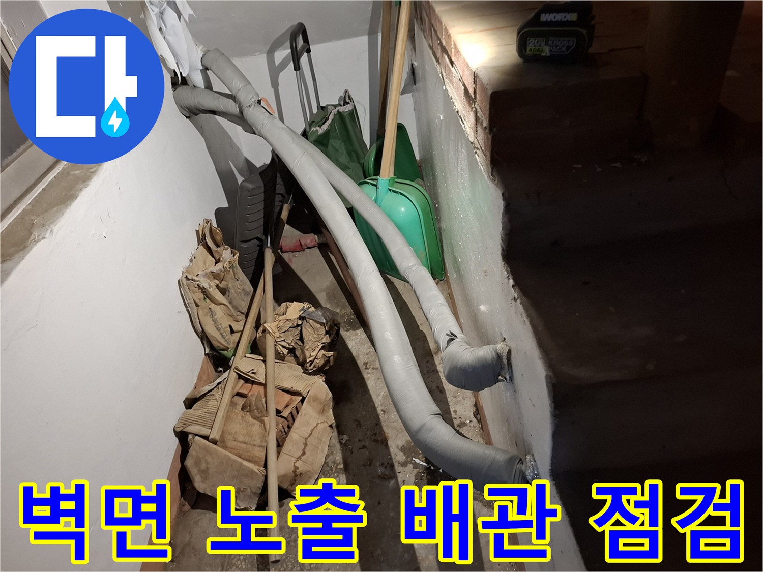 벽면에 설치된 회색 배관과 주변 청소 도구들