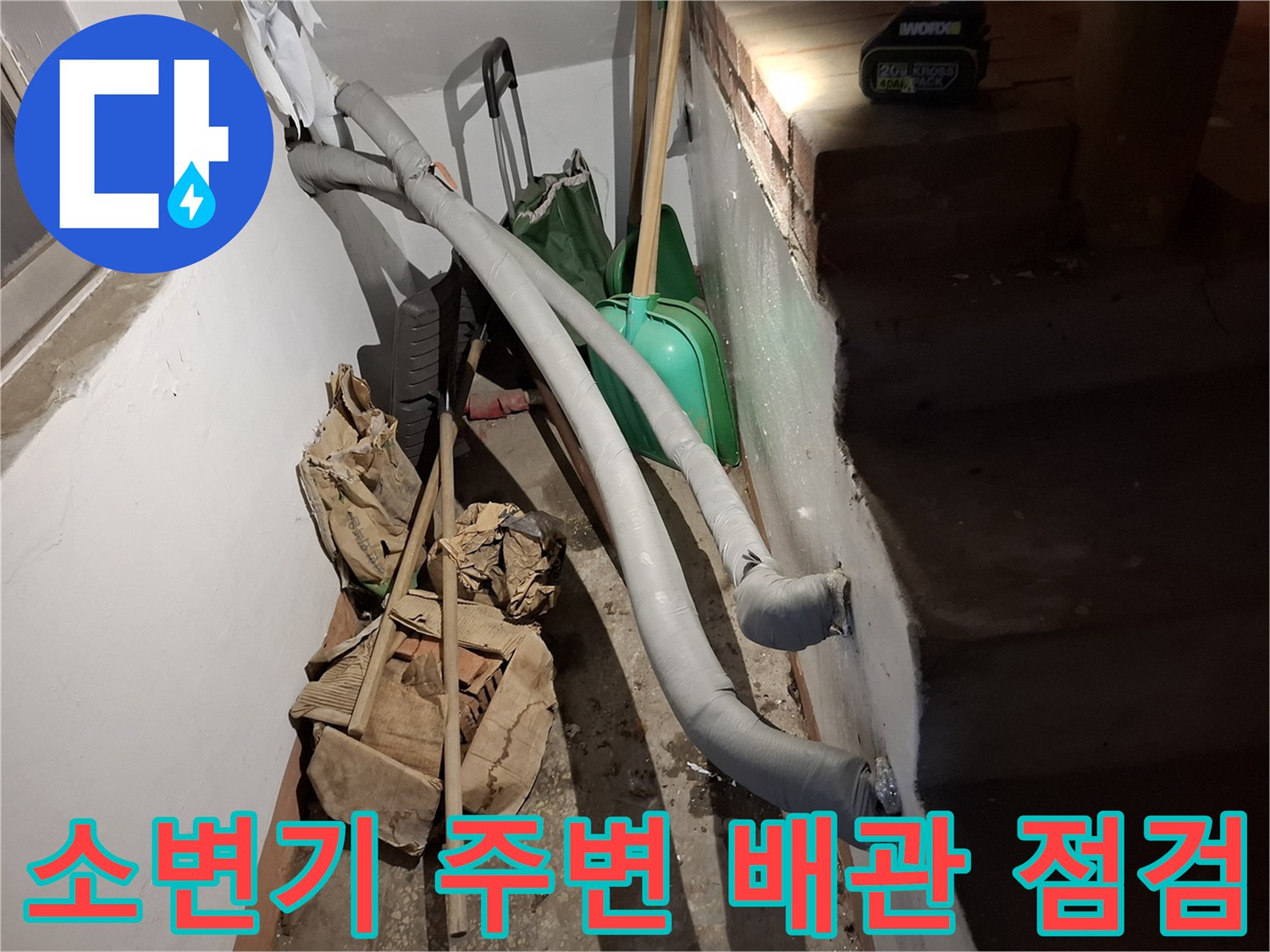 화장실 소변기 근처에 설치된 회색 배관과 작업 도구들