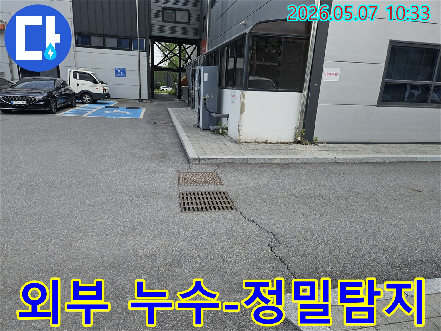 이 이미지는 의정부 만가대길 주차장의 아스팔트 균열과-맨홀-배수구 주변의 지반 문제를 보여주며-외부 누수 정밀 탐지가 필요한 현장입니다.
