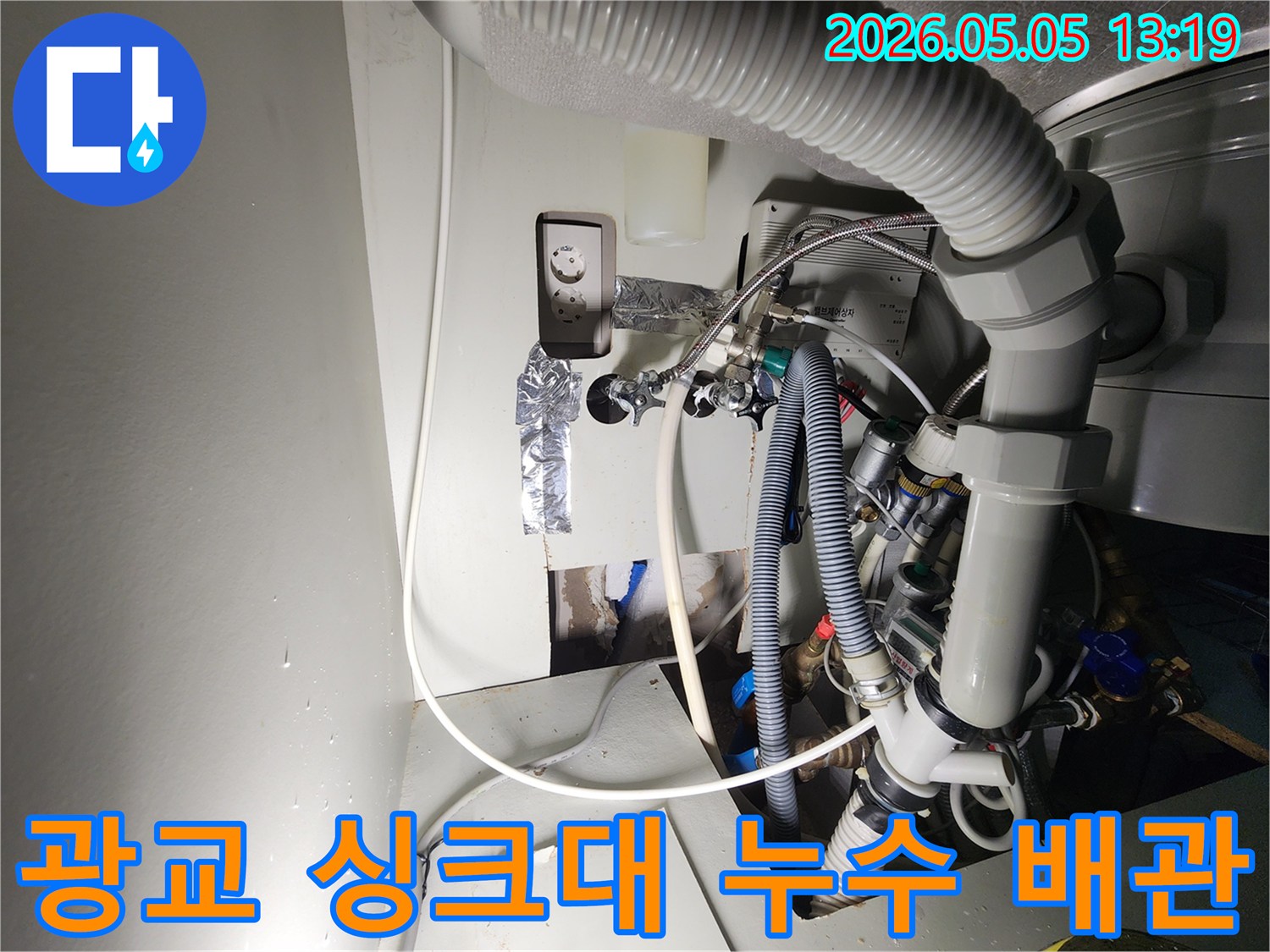 이 이미지는-용인-수지-광교-아파트에서-발생한-싱크대-하부-누수-현장을-보여주며-복잡한-배관과-전기-콘센트-주변에서-물이-새는-모습을-담고-있습니다