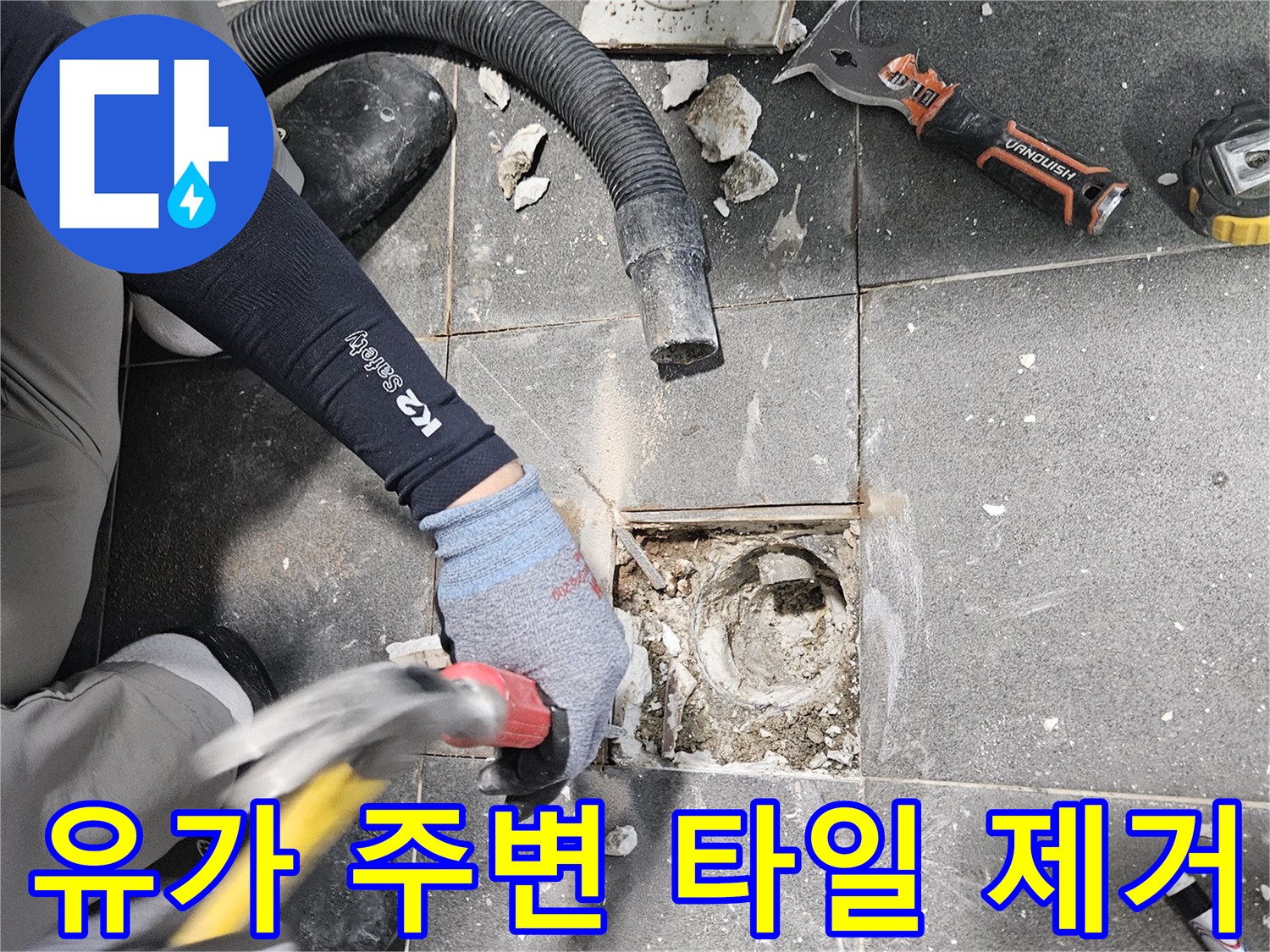 망치를 사용하여 배수구 근처의 젖은 타일을 파쇄하는 공사 장면입니다.