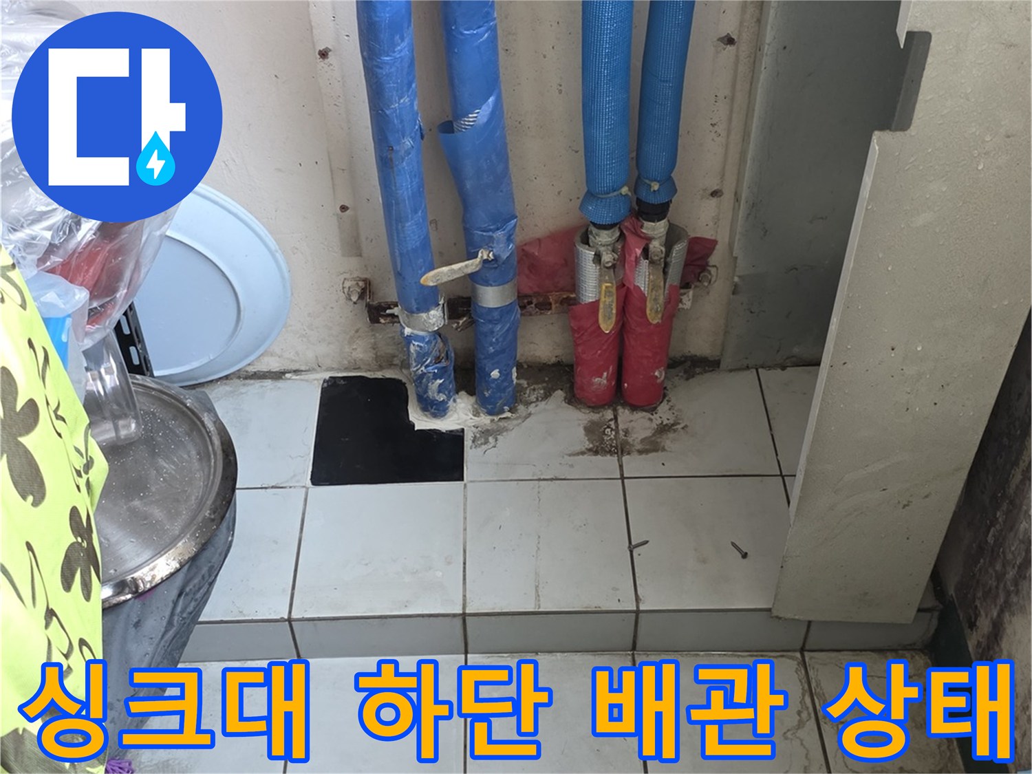 주방 싱크대 하부장 내부의 파란색 보온재가 씌워진 배관과 분배기 연결 부위 모습
