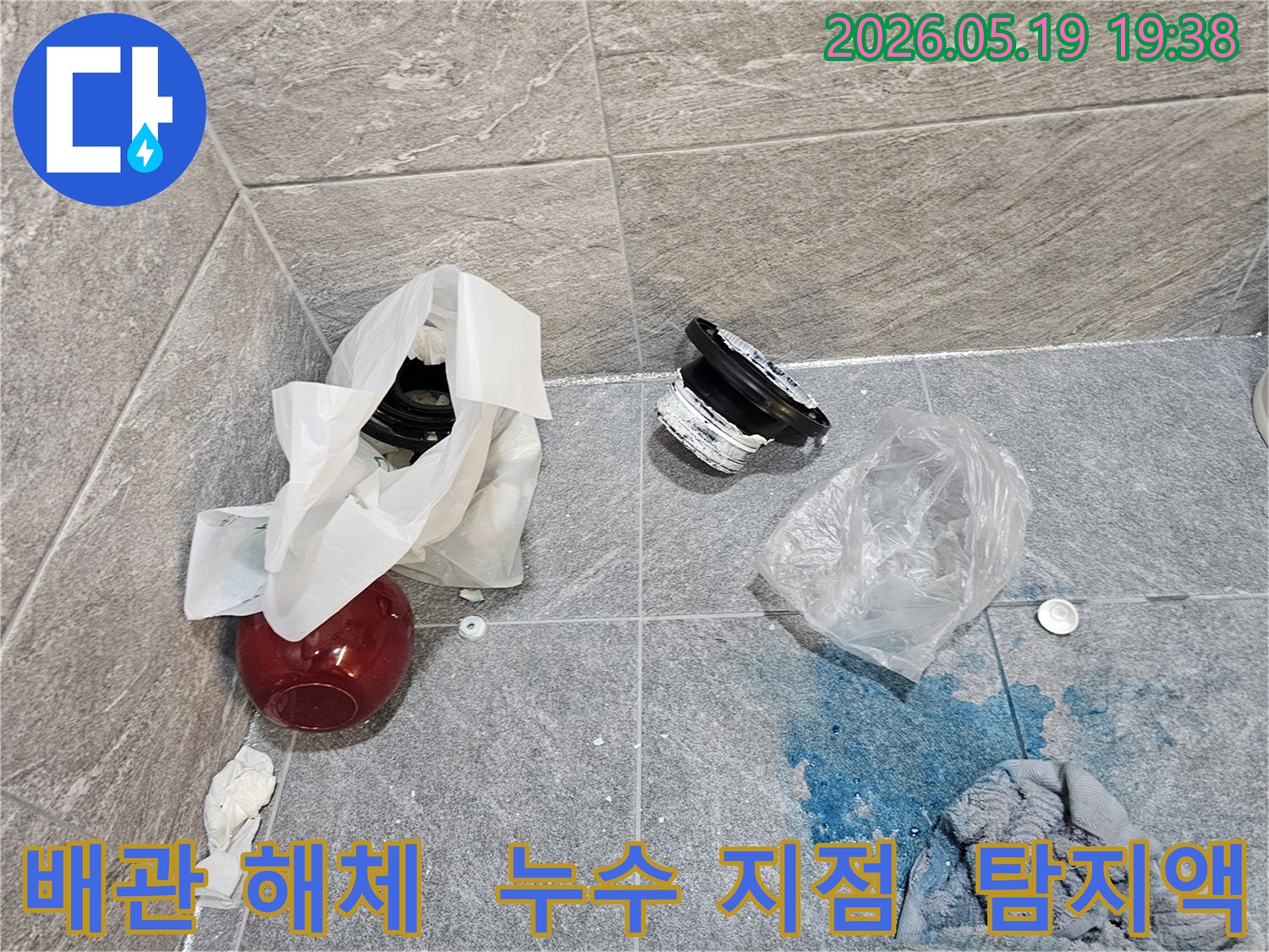 누수 공사 현장에서-파란색 탐지액으로 확인된 누수 지점과-교체를 위해 해체된 배관 부품들이 바닥에 놓여 있습니다