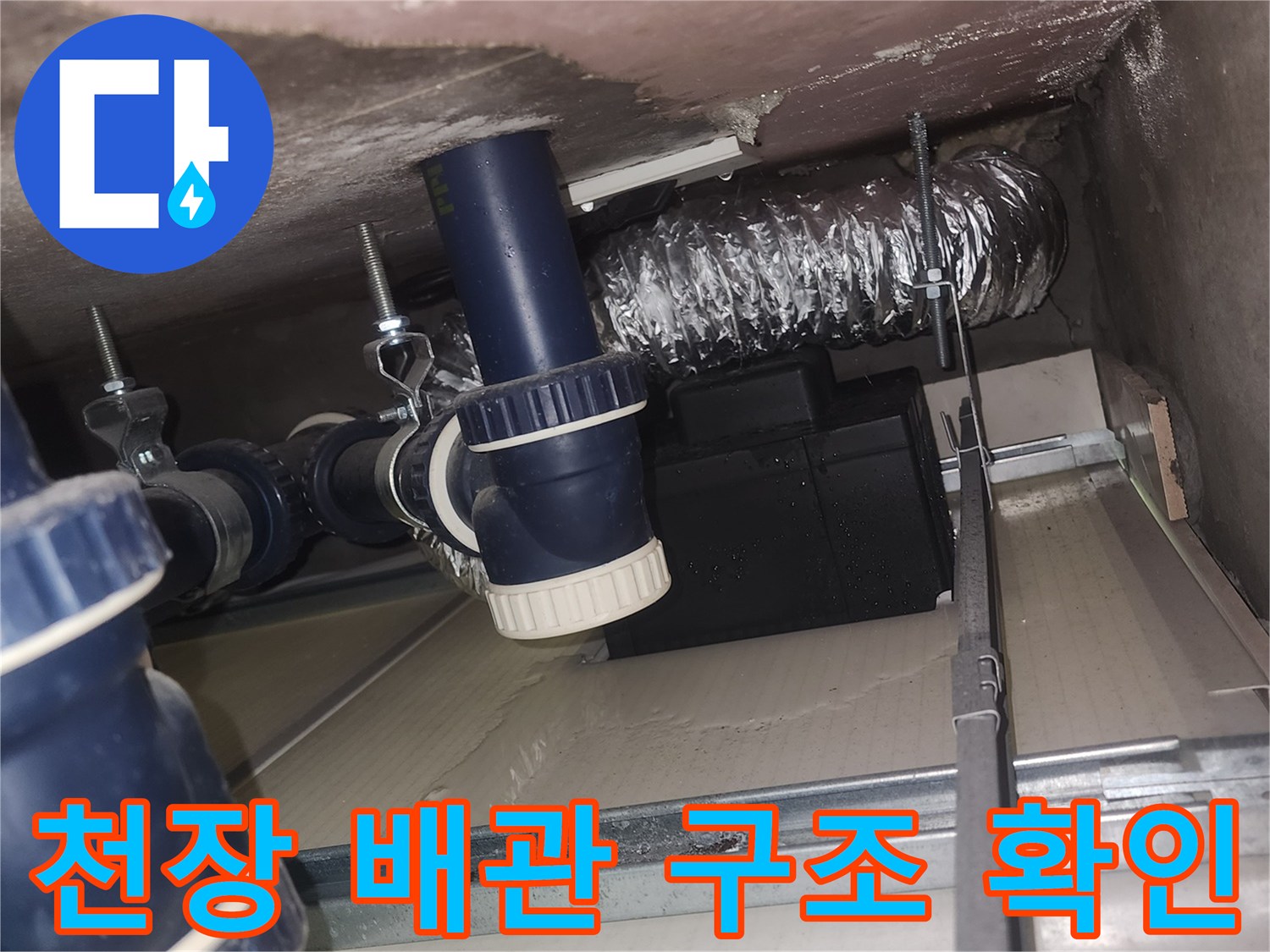 욕실 천장 내부에 노출된 파란색 배수 부속과 은색 배관