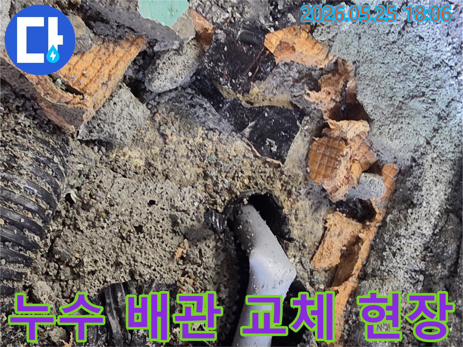 파쇄된 바닥 아래에서 발견된 젖은 배관과 주변의 흙-콘크리트 조각들은-누수 수리를 위한 배관 교체 작업을 보여줍니다.