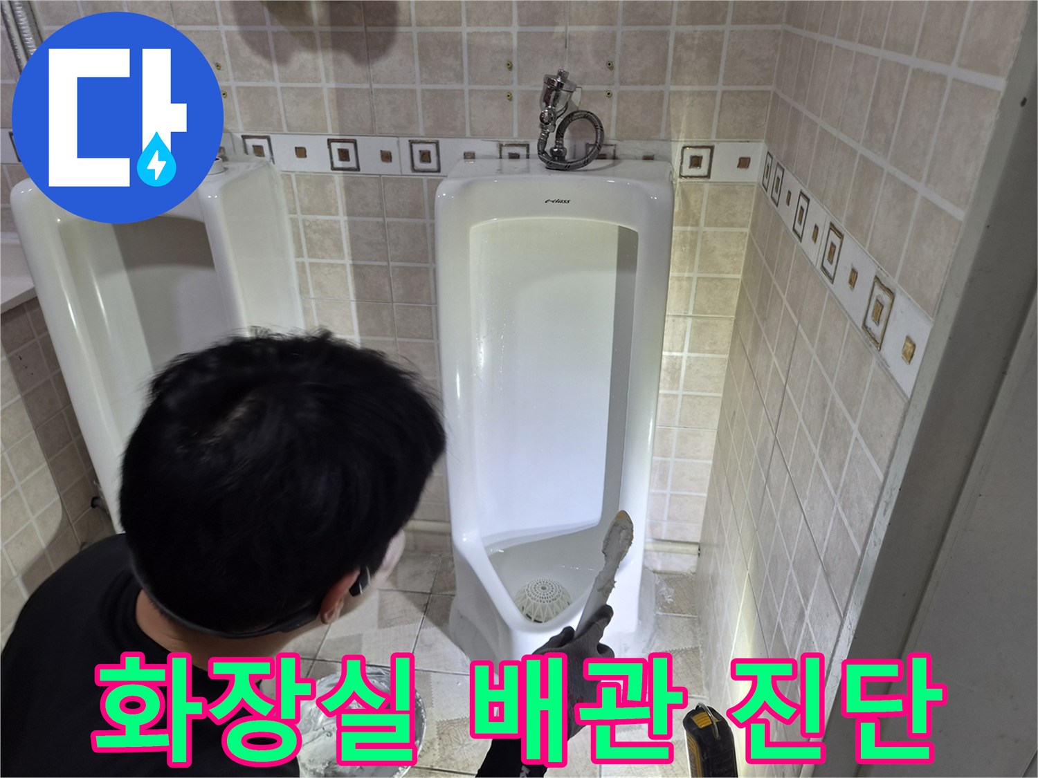 소변기 아래쪽 배관 연결부와 주변 타일 상태를 점검하는 엔지니어