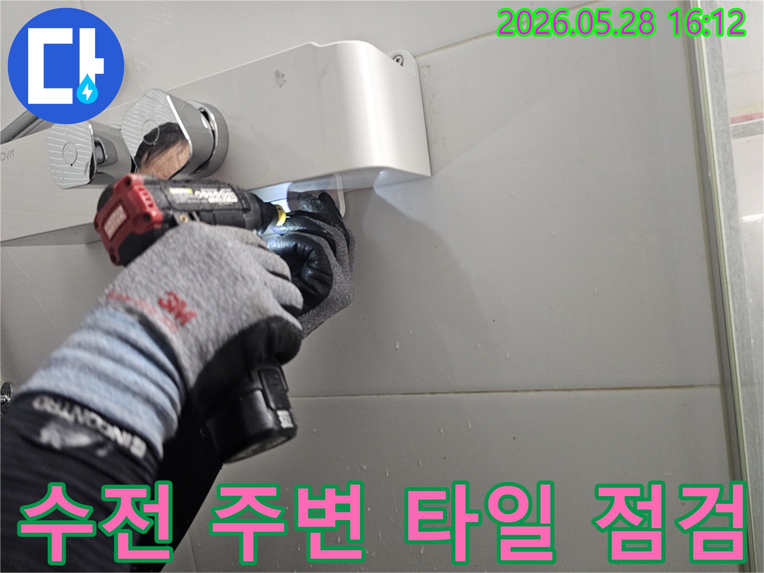 전문 기술자가-보호 장갑을 착용하고-전동 공구로-샤워기 수전 주변의-타일 상태를-정밀하게-점검하는-모습입니다