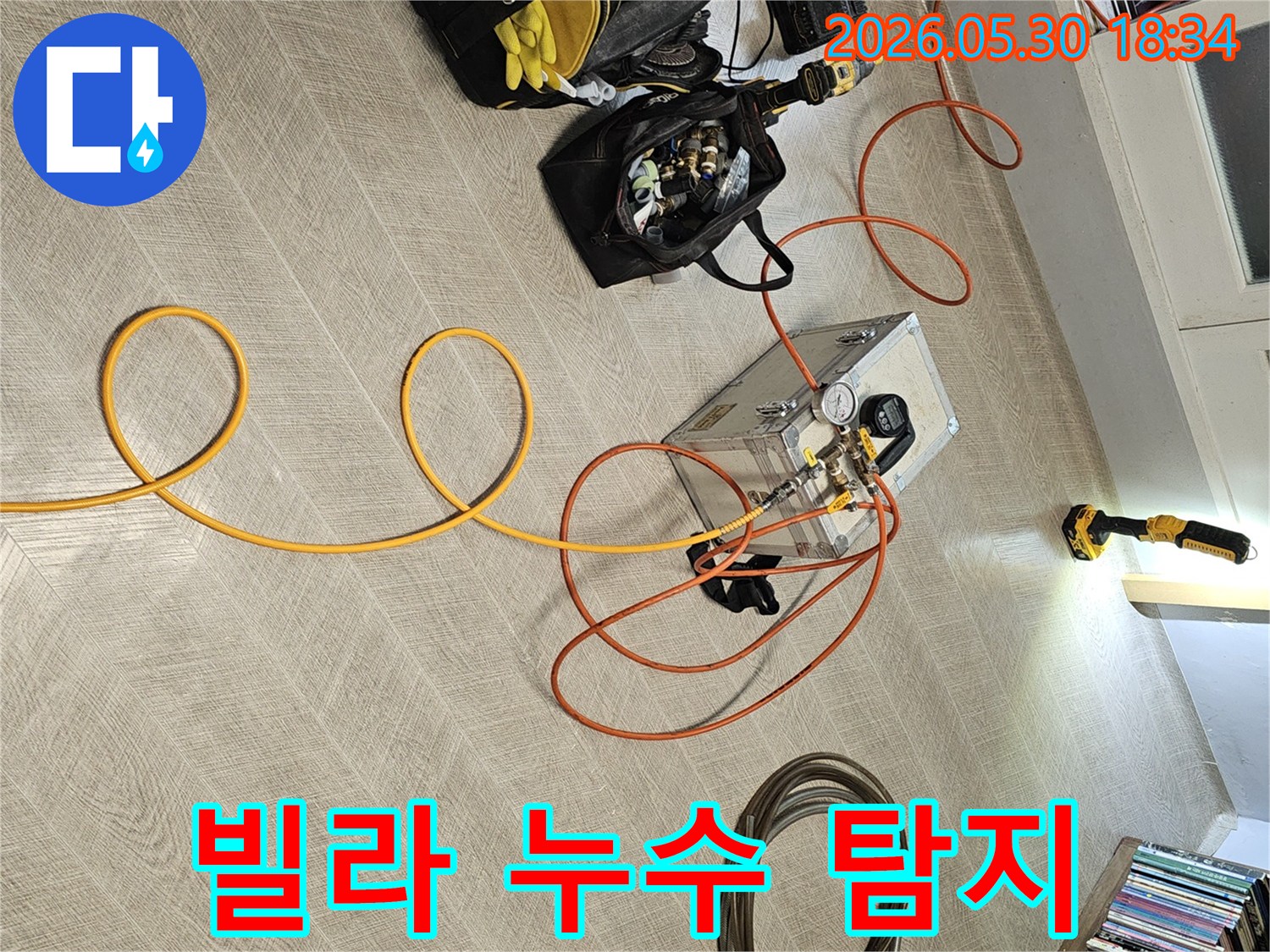 실내 바닥에 설치된 누수 탐지 장비와-다양한 연결 호스-그리고 작업 도구들이-누수 진단을 위해 준비된 장면입니다.