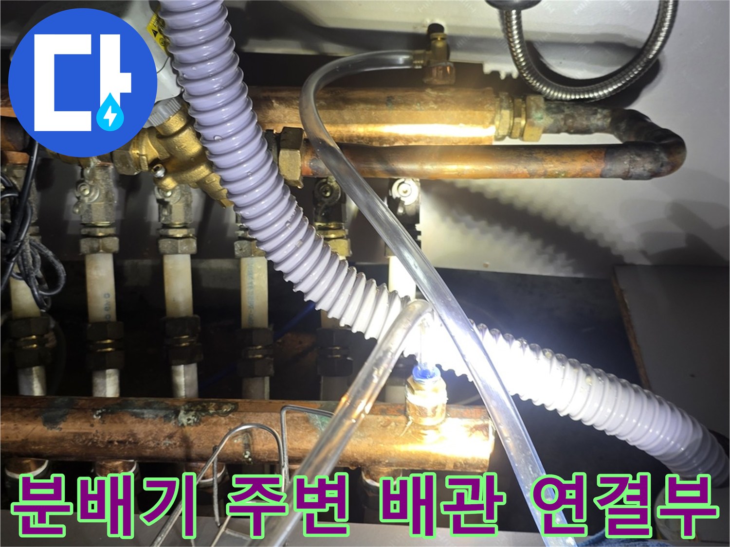 싱크대 하부장 내부에 노출된 보일러 분배기와 금속 배관들의 모습