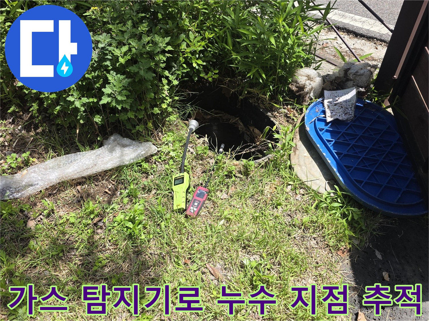 풀숲 사이 맨홀 근처에서 배관의 가스 누출을 확인하는 전문 장비 모습입니다.