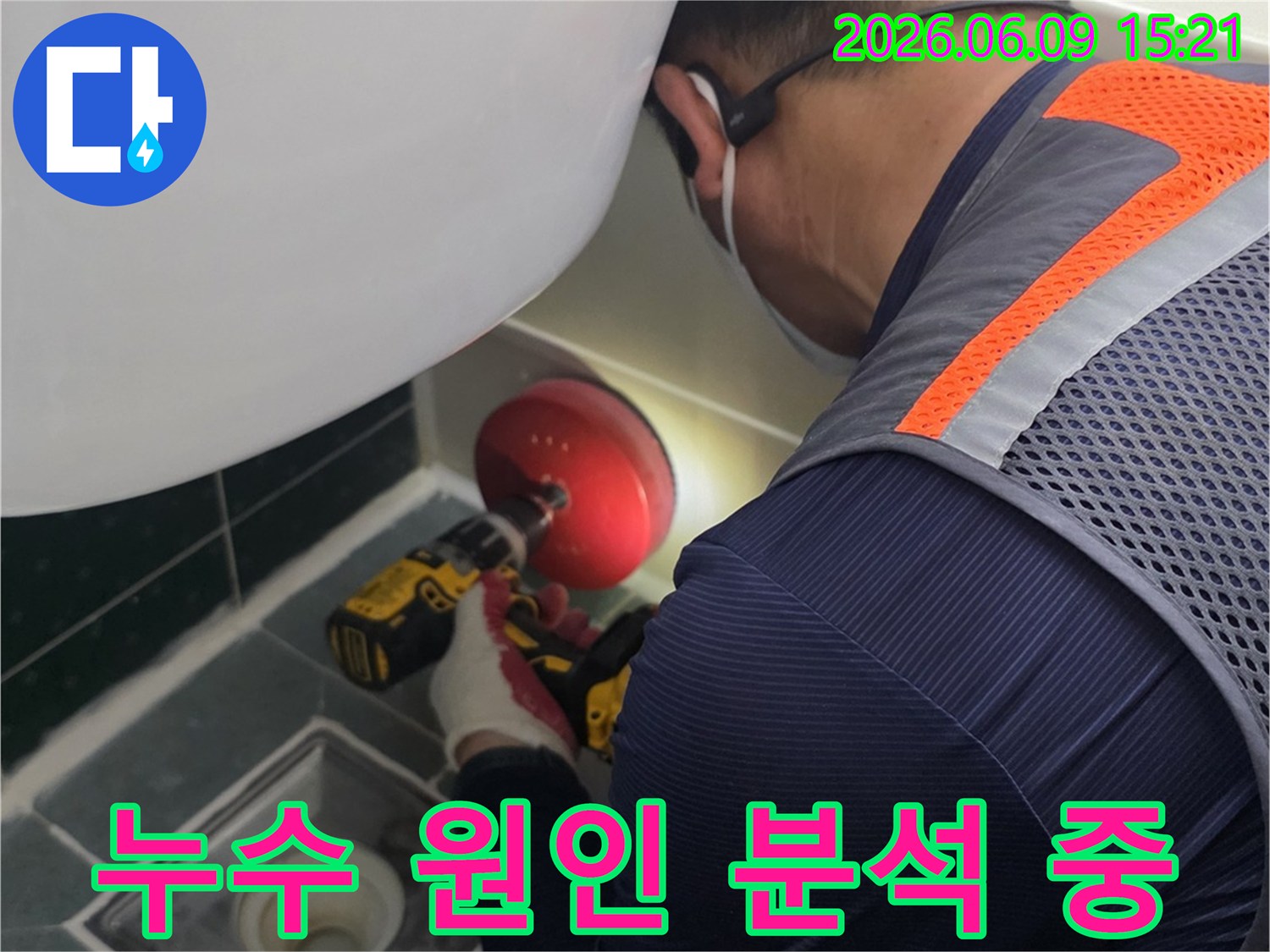 안전-조끼를-입은-전문가가-욕실-배수구-근처의-누수-지점을-정확히-파악하기-위해-전동-공구를-사용하여-작업하는-장면