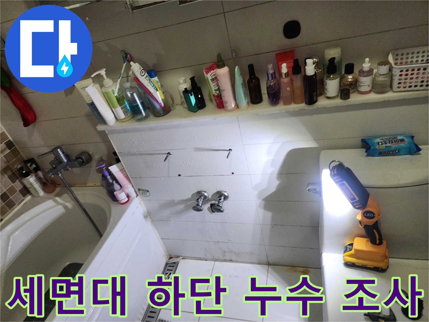 손전등으로 세면대 아래쪽 배관 연결부를 면밀히 관찰하는 모습