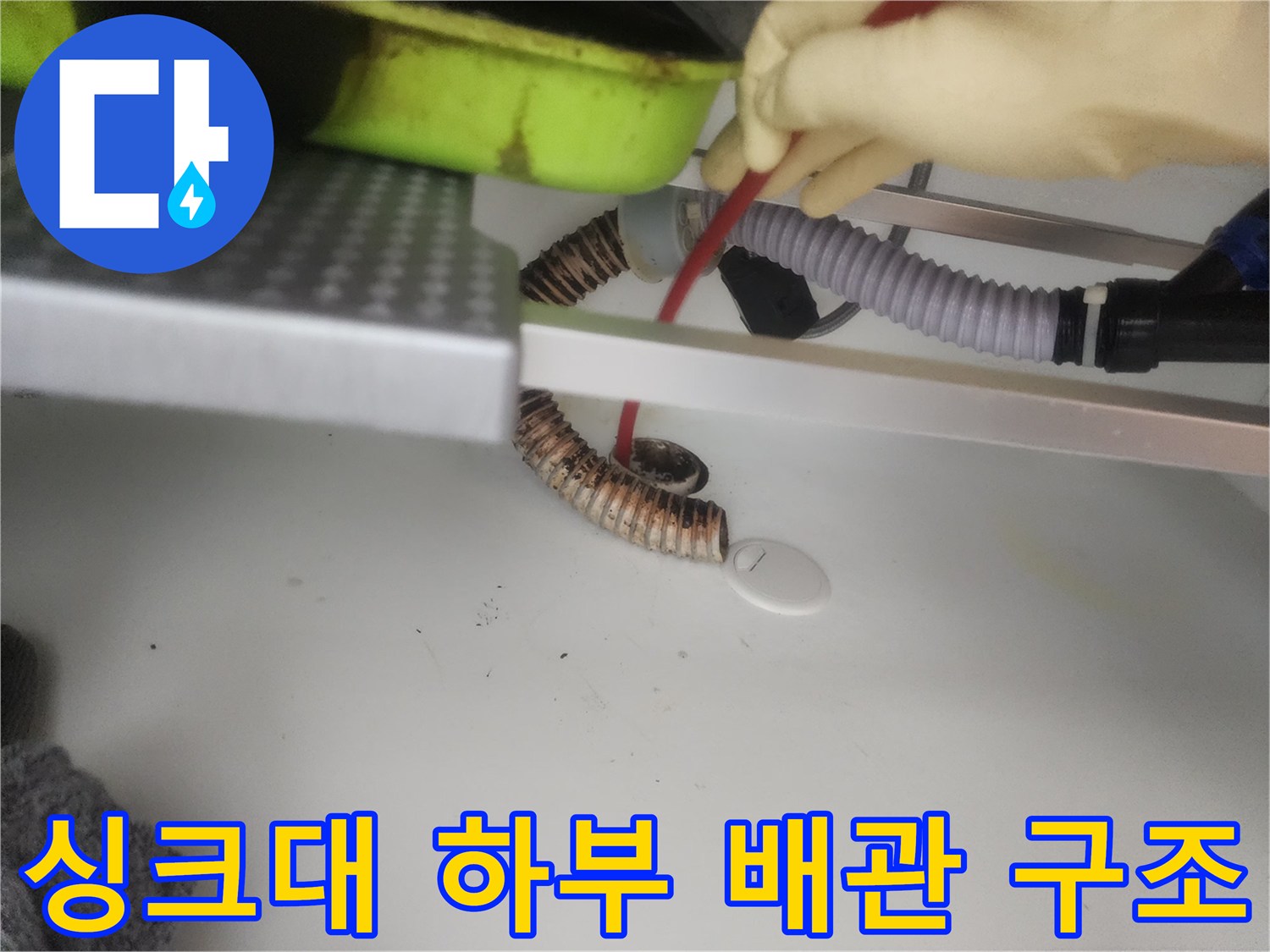 싱크대 아래쪽의 굴곡진 주름 배관과 수평으로 놓인 구조물입니다.