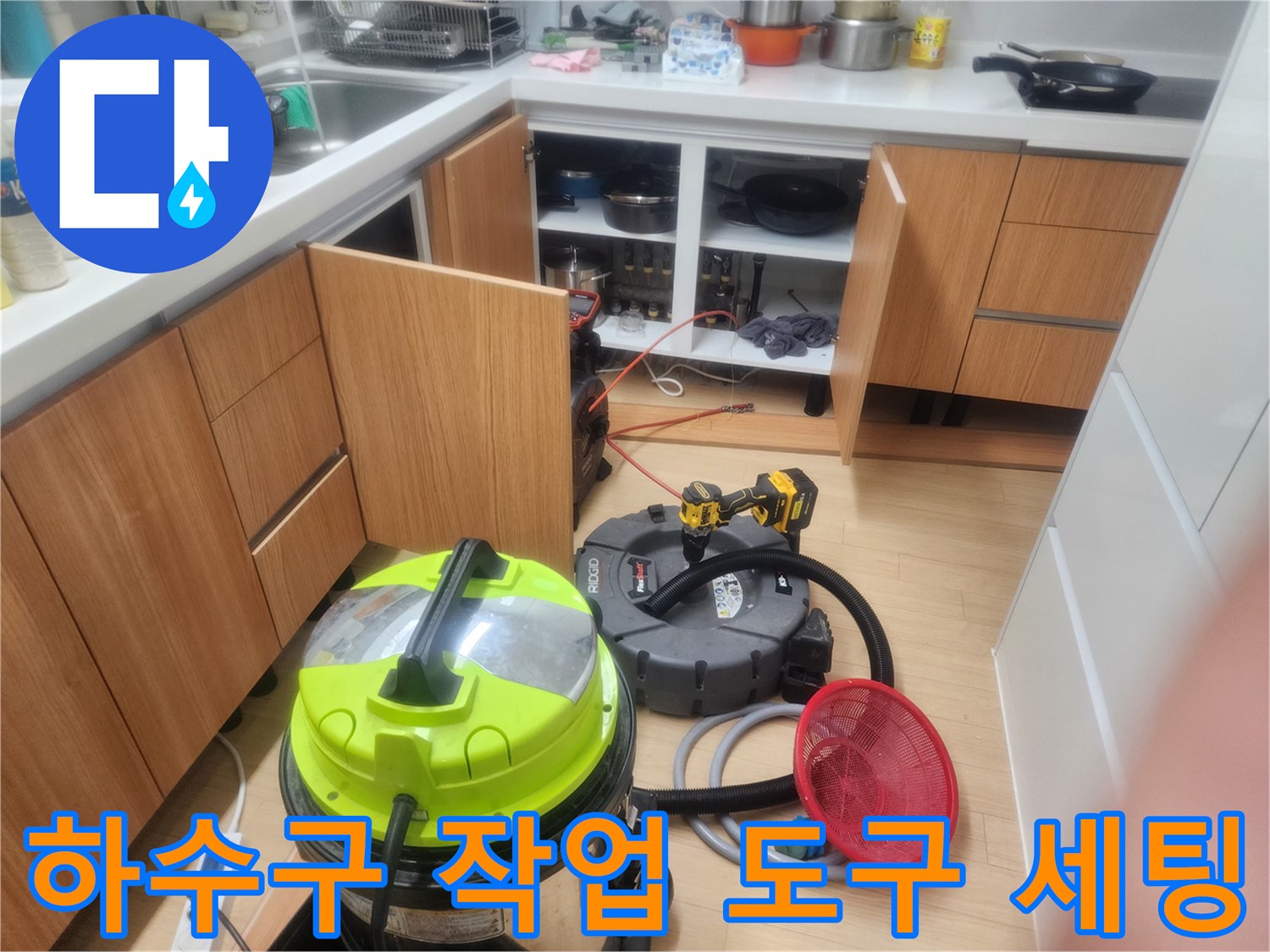 싱크대 하부장 앞 배관 작업을 위해 준비된 청소용 진공 장비와 호스