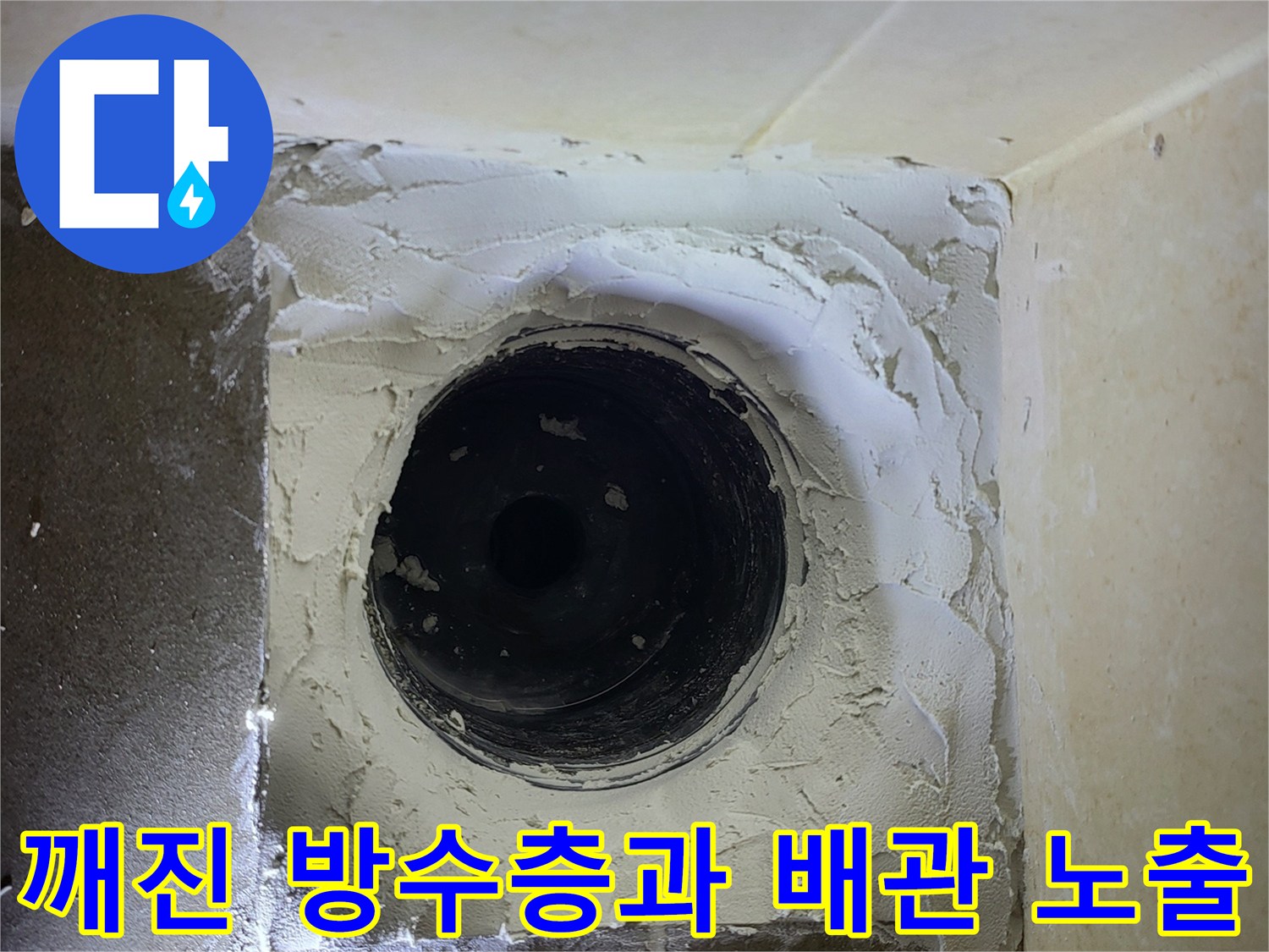 배관 주변의 파손된 타일과 노출된 시멘트 부위입니다.