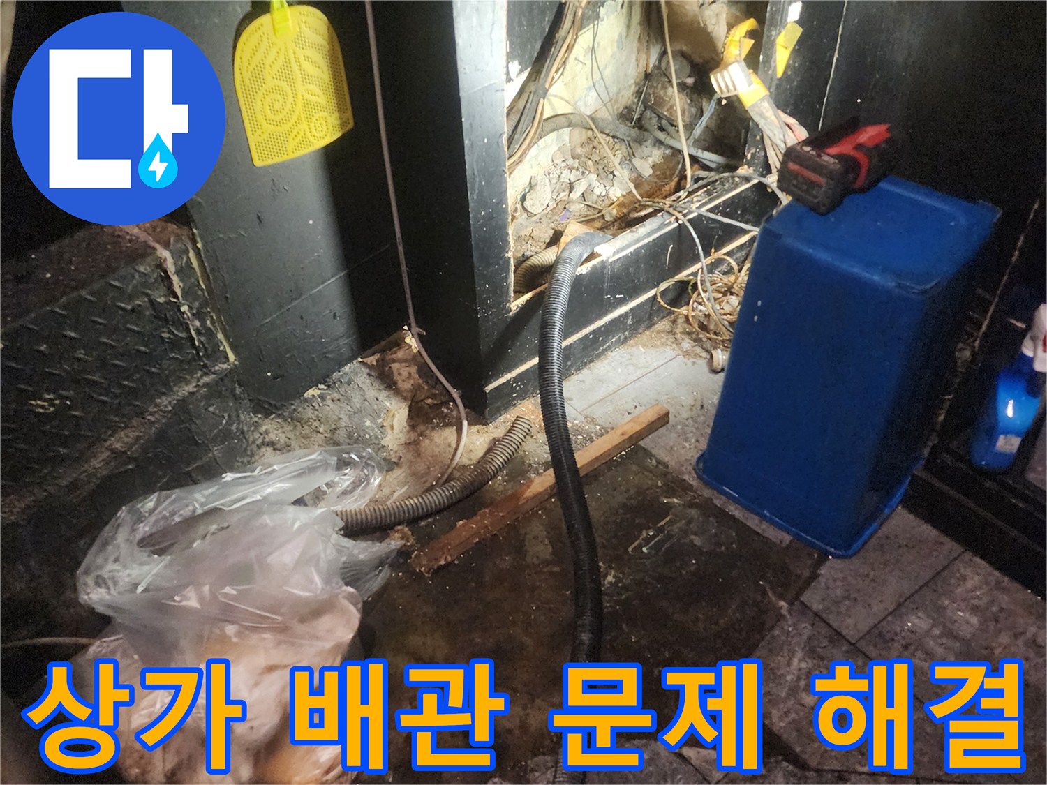 어두운 상가 바닥 아래에서 복잡하게 얽힌 배관과 전선-그리고 누수로 인해 젖은 바닥을 보여주며 문제 해결을 위한 작업을 진행하는 현장
