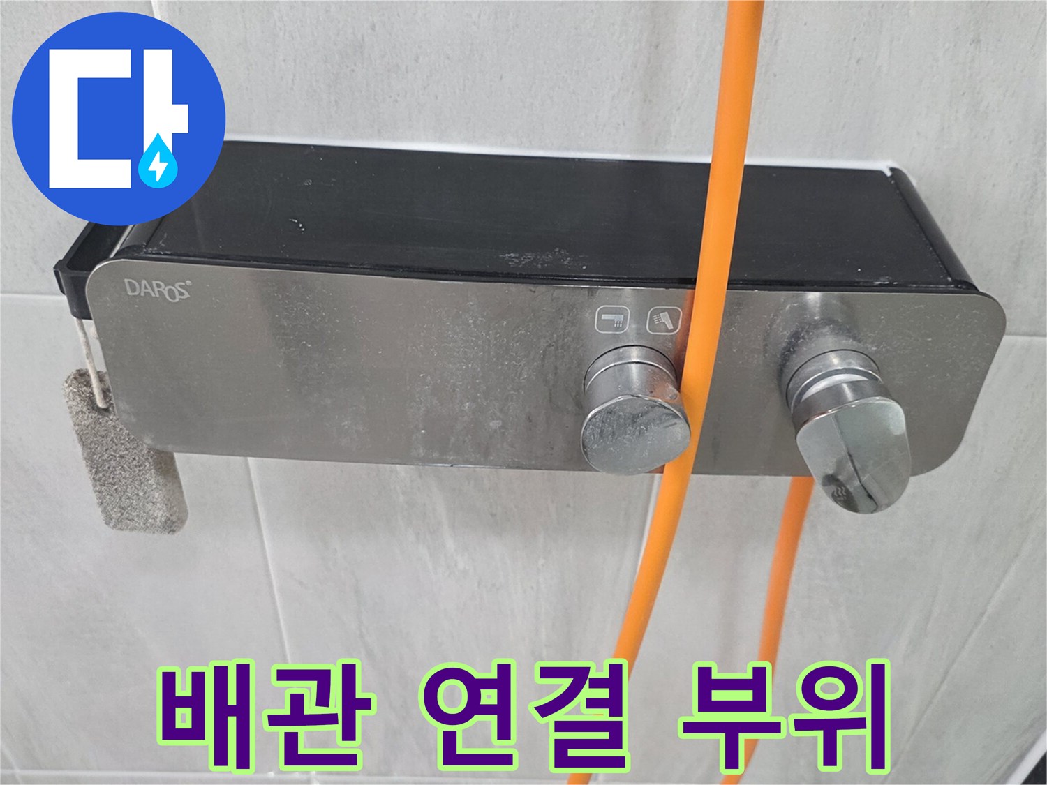 은색 수전과 주황색 호스가 연결된 벽면 모습