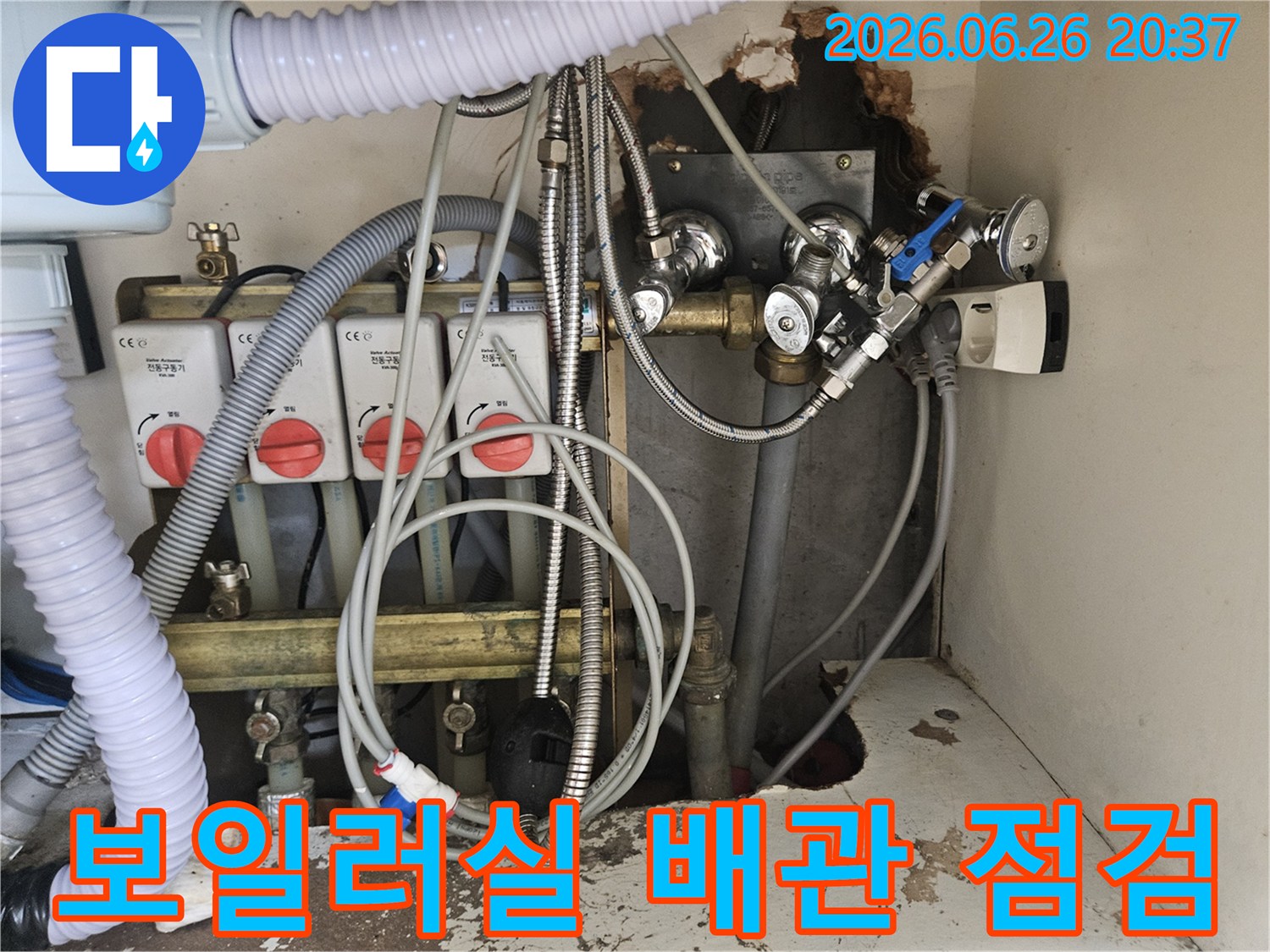 이 이미지는-아파트 보일러실의-복잡한 배관과-밸브-그리고-전기 콘센트가-보이는-누수 현장의-전반적인 모습을-제공합니다