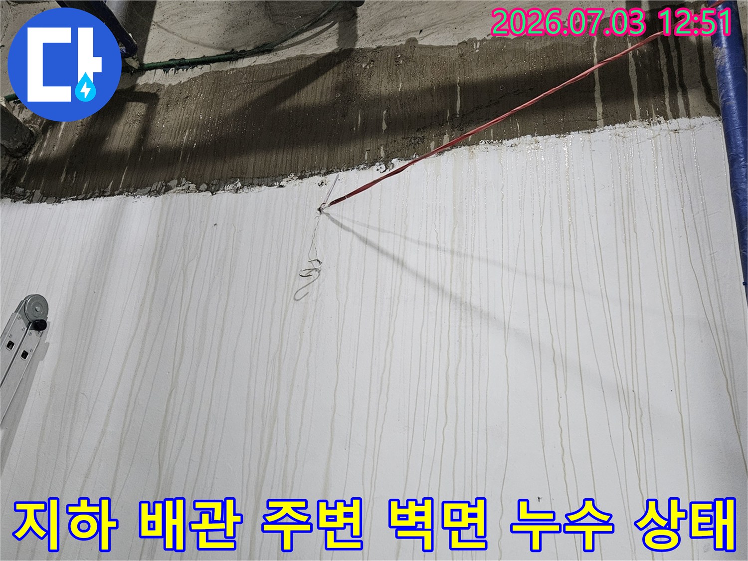 파란색 보온재가 감싸진 배관 옆으로-물이 흘러내려 얼룩진 지하 1층의 흰색 벽면과 천장 경계부