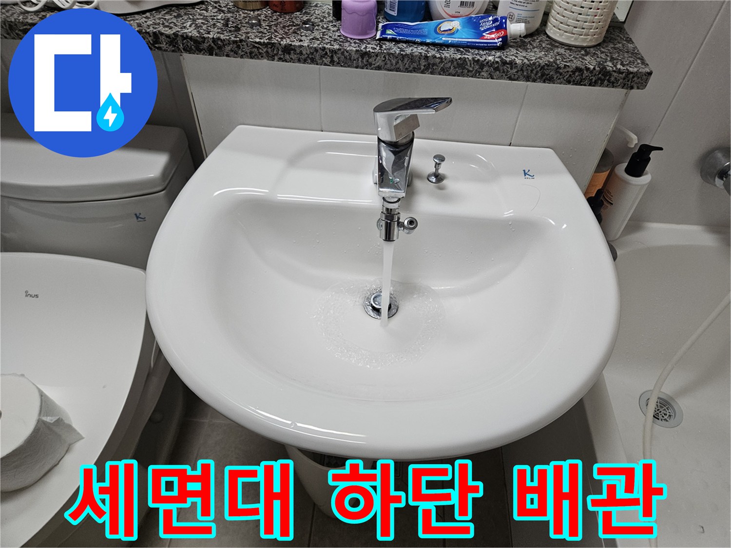 하얀색 세면대 아래에 위치한 은색 수전 부속품입니다.