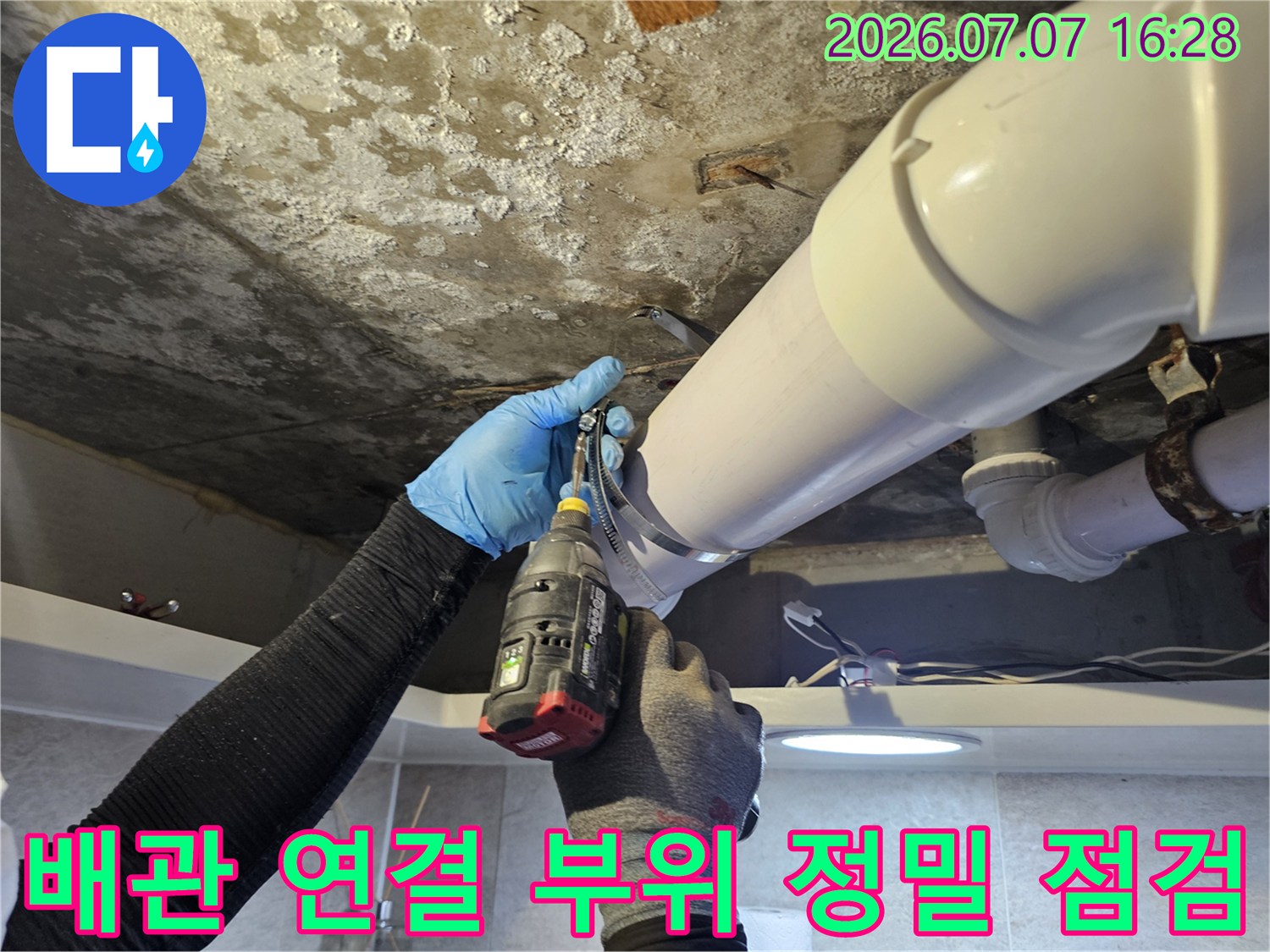 장갑을 낀 작업자가 화장실 천장 안쪽의 배출용 파이프와 부속물들을 상세히 살피는 장면
