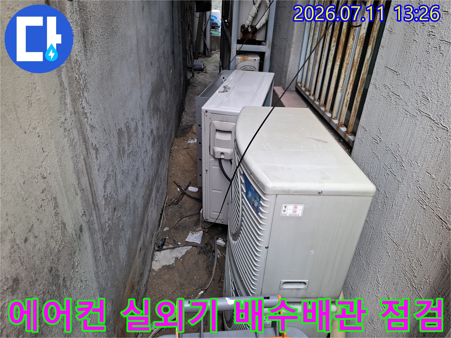 실외기들이 설치된 좁은 공간에서 에어컨 드레인 배관을 정밀하게 점검하는 모습