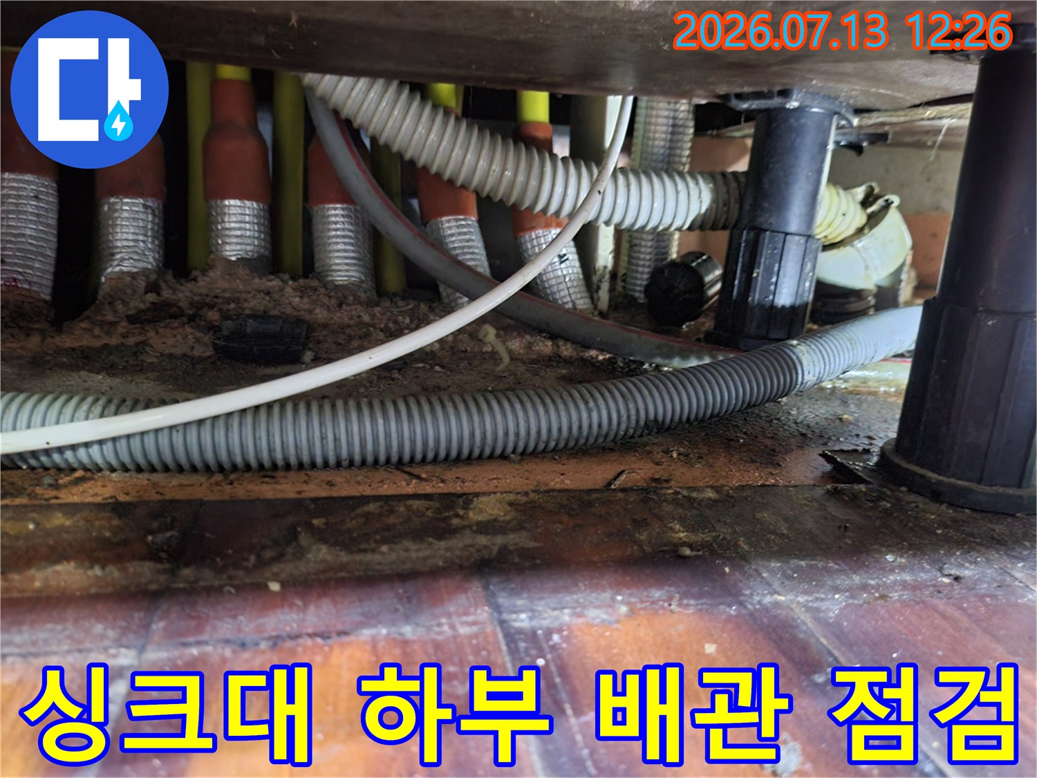 싱크대 아래에 위치한 여러 개의 회색 배관과 보온재가 덮인 모습