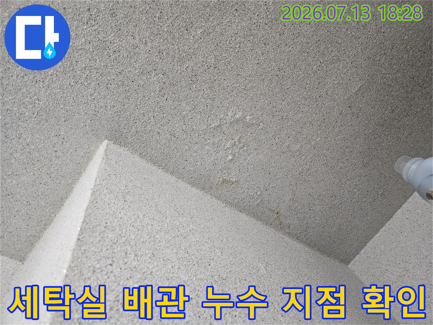 거친 질감의 세탁실 천장면과 노출된 배관 연결부 근처의 습기 흔적